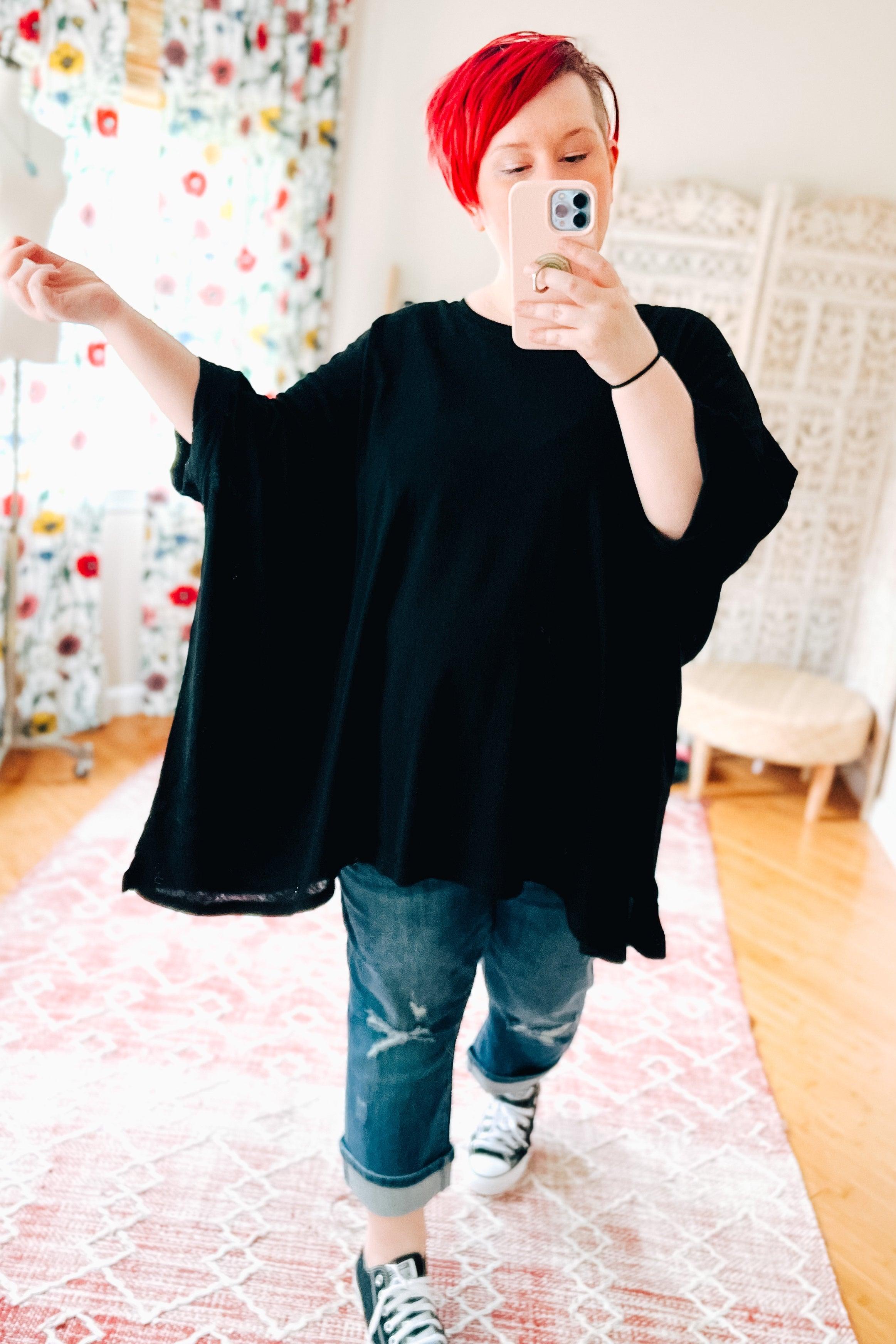 Woman with red hair wearing loose black All My Life Boxy Top taking mirror selfie indoors