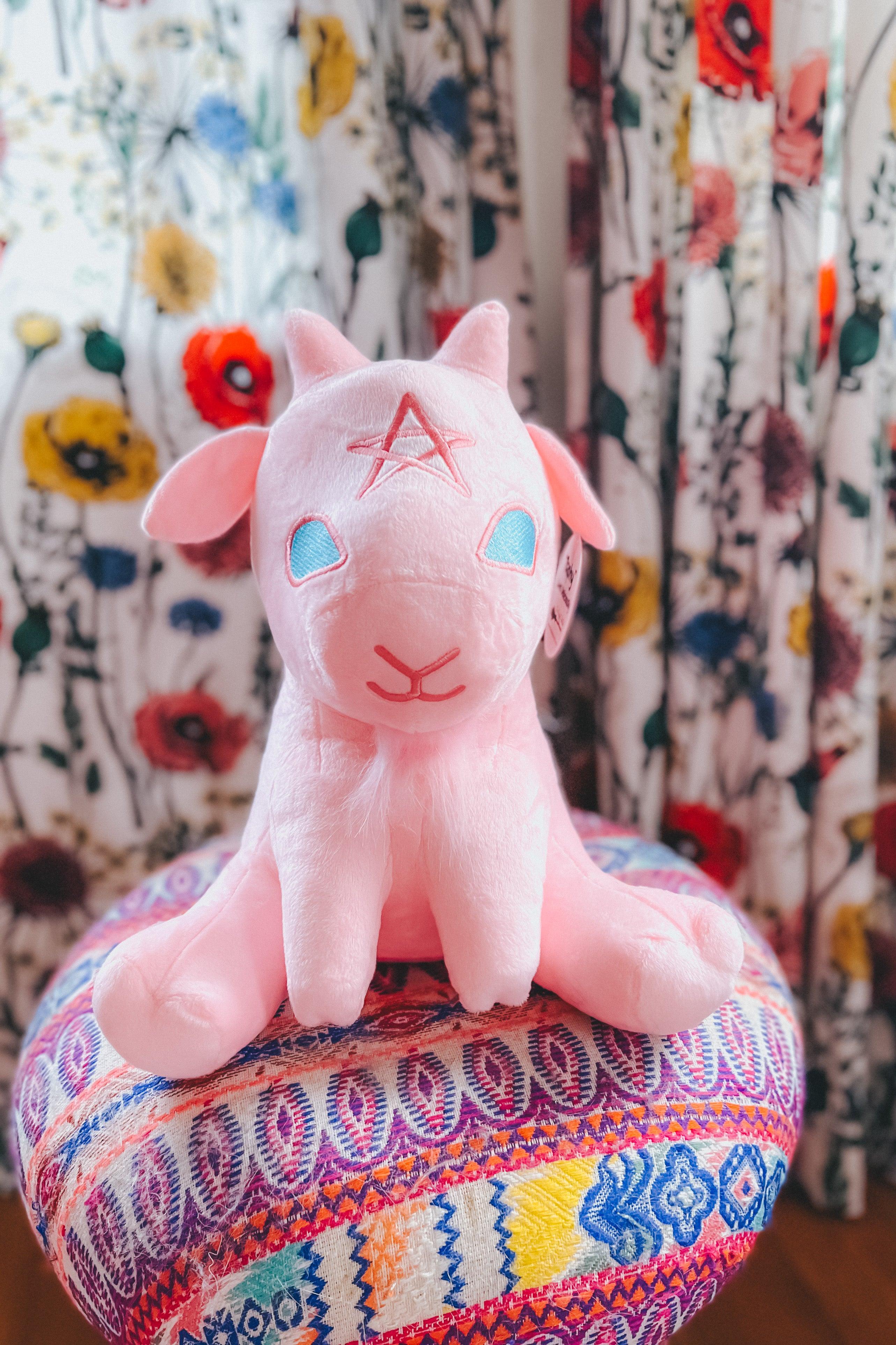 Pink Witchy Baby Goat plushie with star forehead sitting on colorful patterned fabric round cushion.