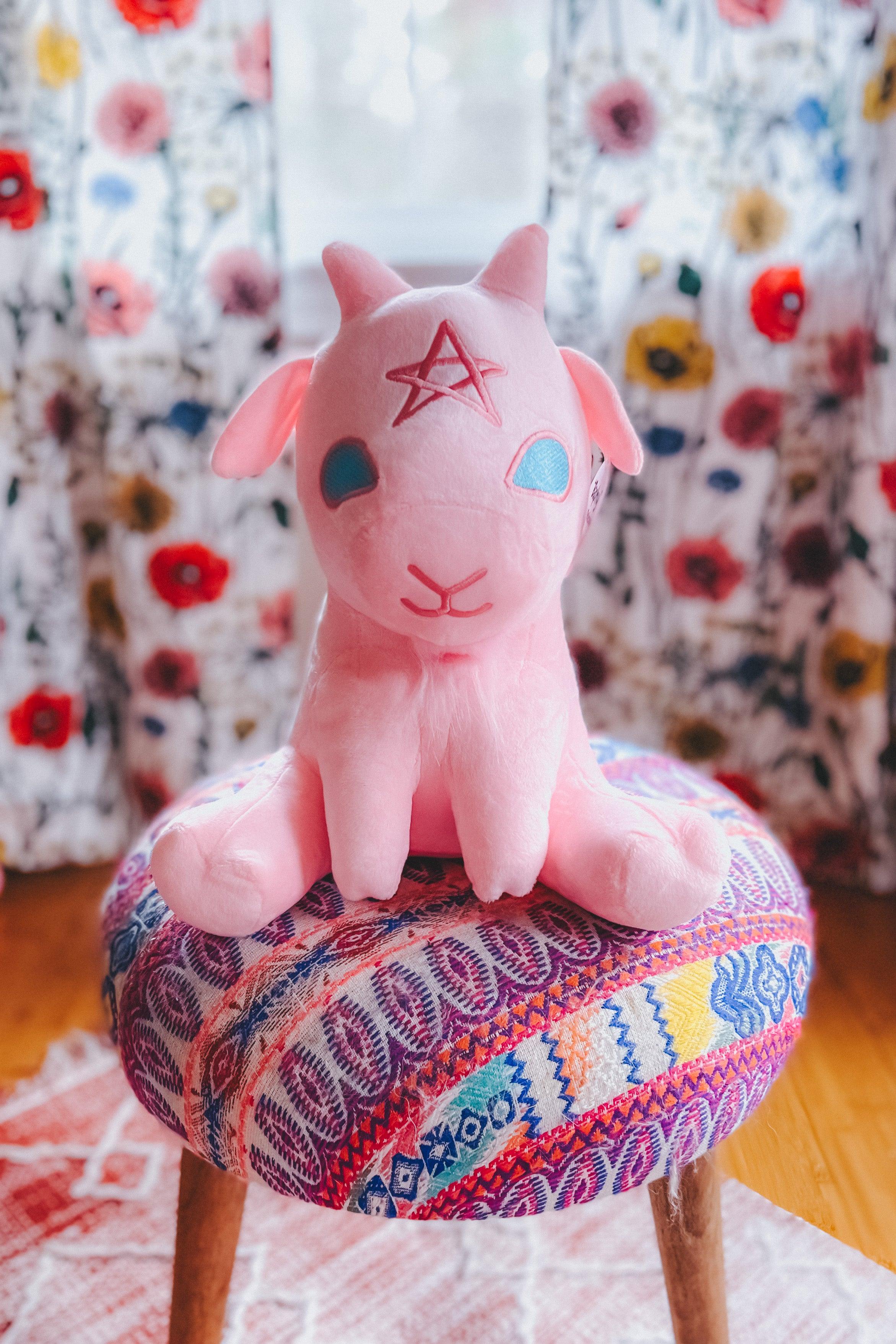 Cotton candy pink Baphy Witchy Baby Goat plush with star forehead sitting on colorful patterned round stool indoors