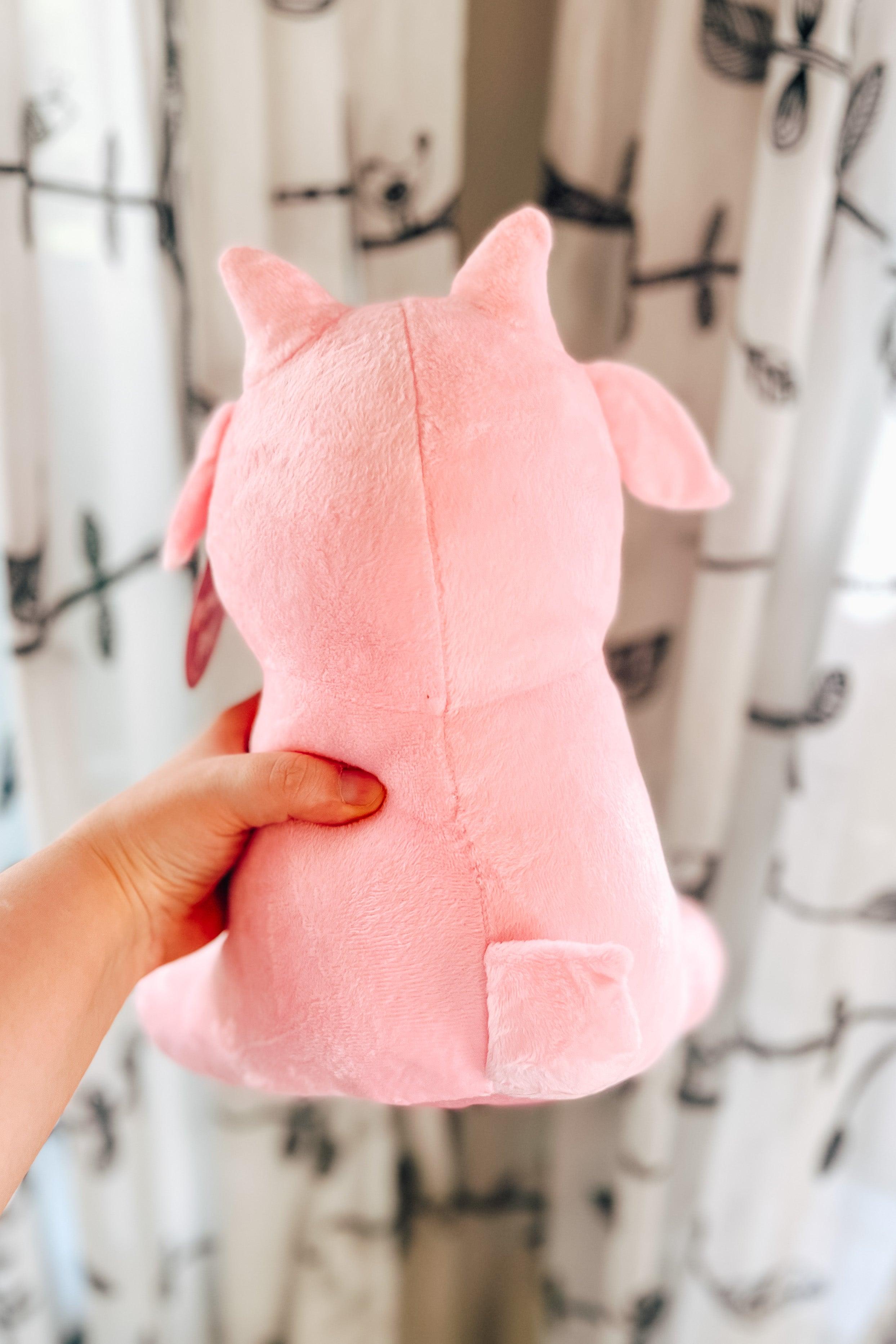 Hand holding cotton candy pink Baphy Witchy Baby Goat plush showing back with small tail and ears against patterned curtain background