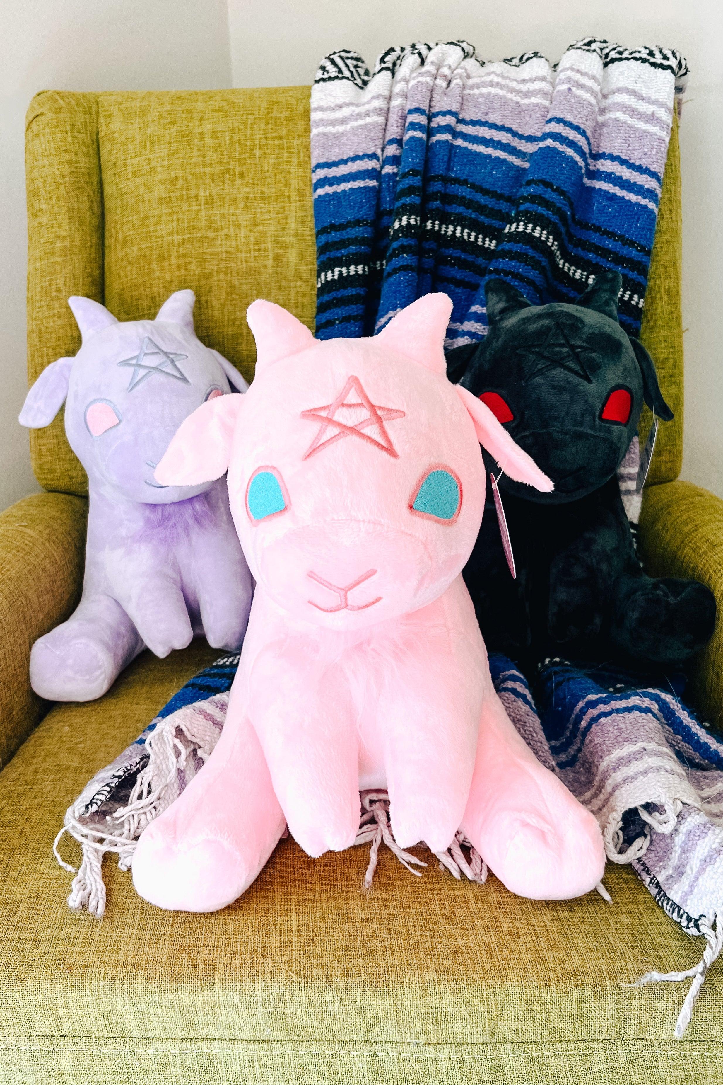 Cotton candy pink Baphy Witchy Baby Goat plush with aqua eyes and pink star sitting on green chair with colorful blanket behind