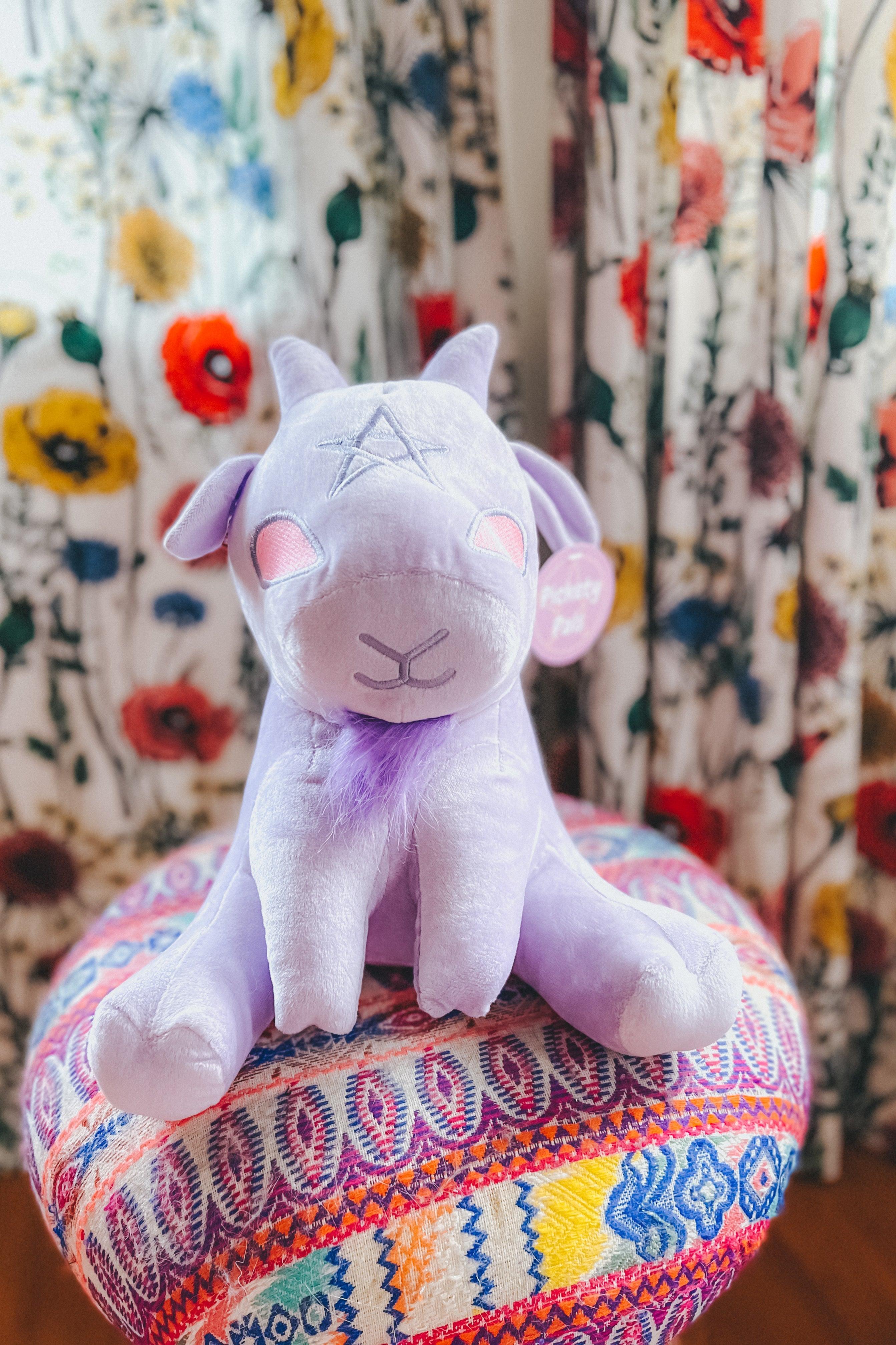 Lavender Baphy Witchy Baby Goat plush with embroidered star sitting on colorful patterned round cushion in cozy room