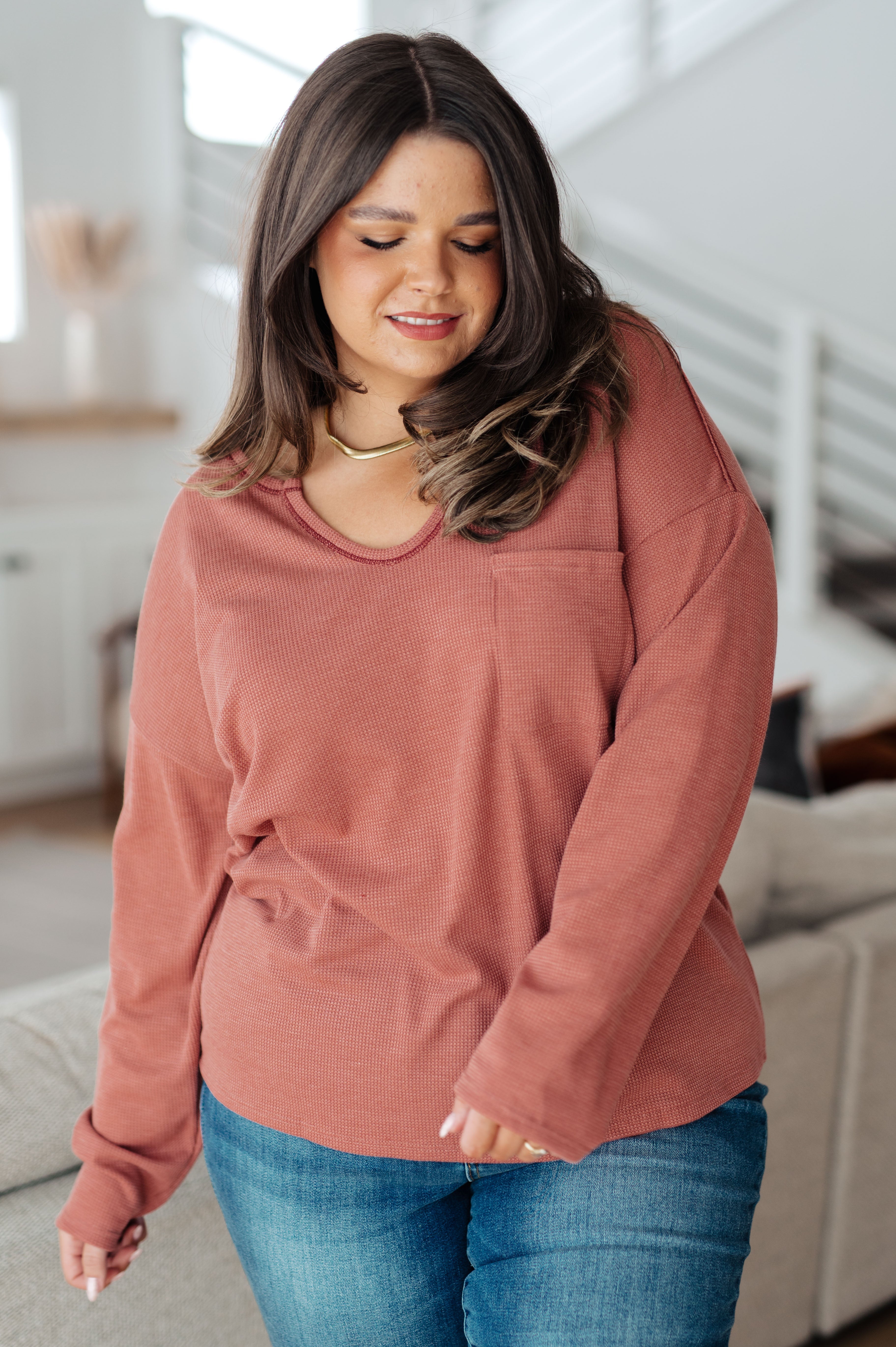 Plus-size woman wearing rust-colored Behind The Scenes waffle knit top with rounded neckline and pocket indoors