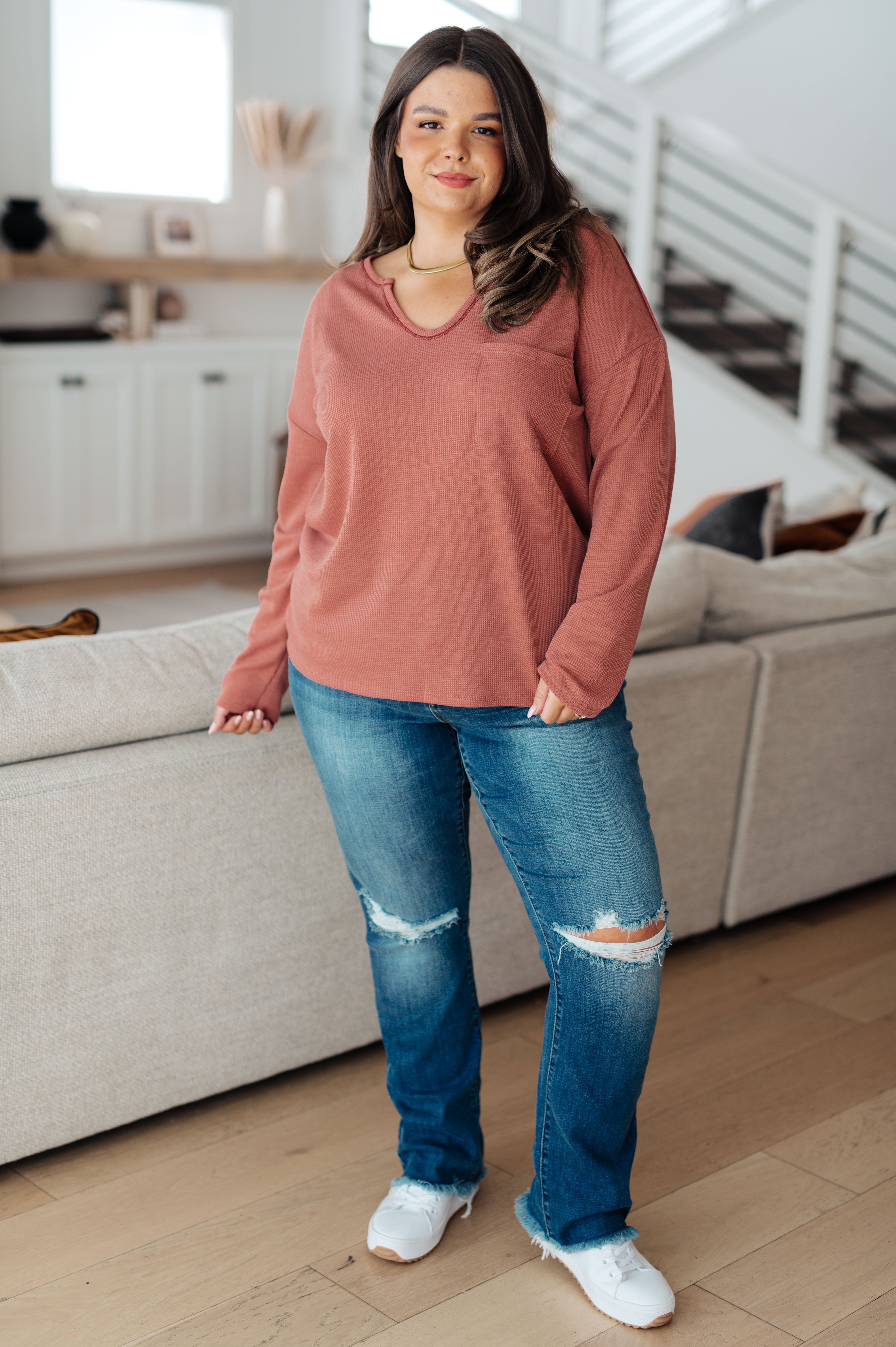 Plus-size model wearing rust-colored Behind The Scenes waffle knit top with v-neck and chest pocket standing in bright living room