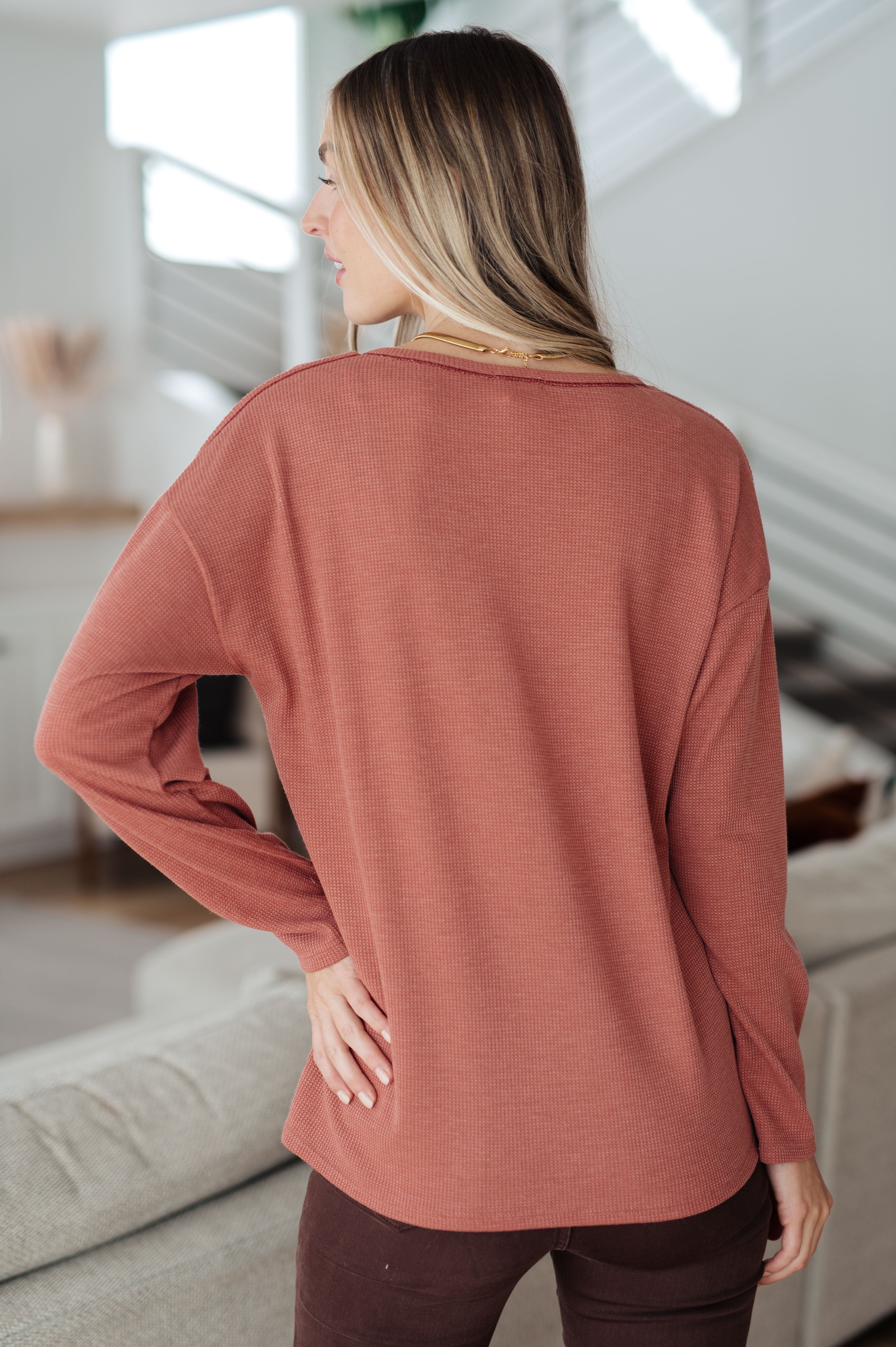 Woman modeling Behind The Scenes rust-colored waffle knit top from back in modern living room setting