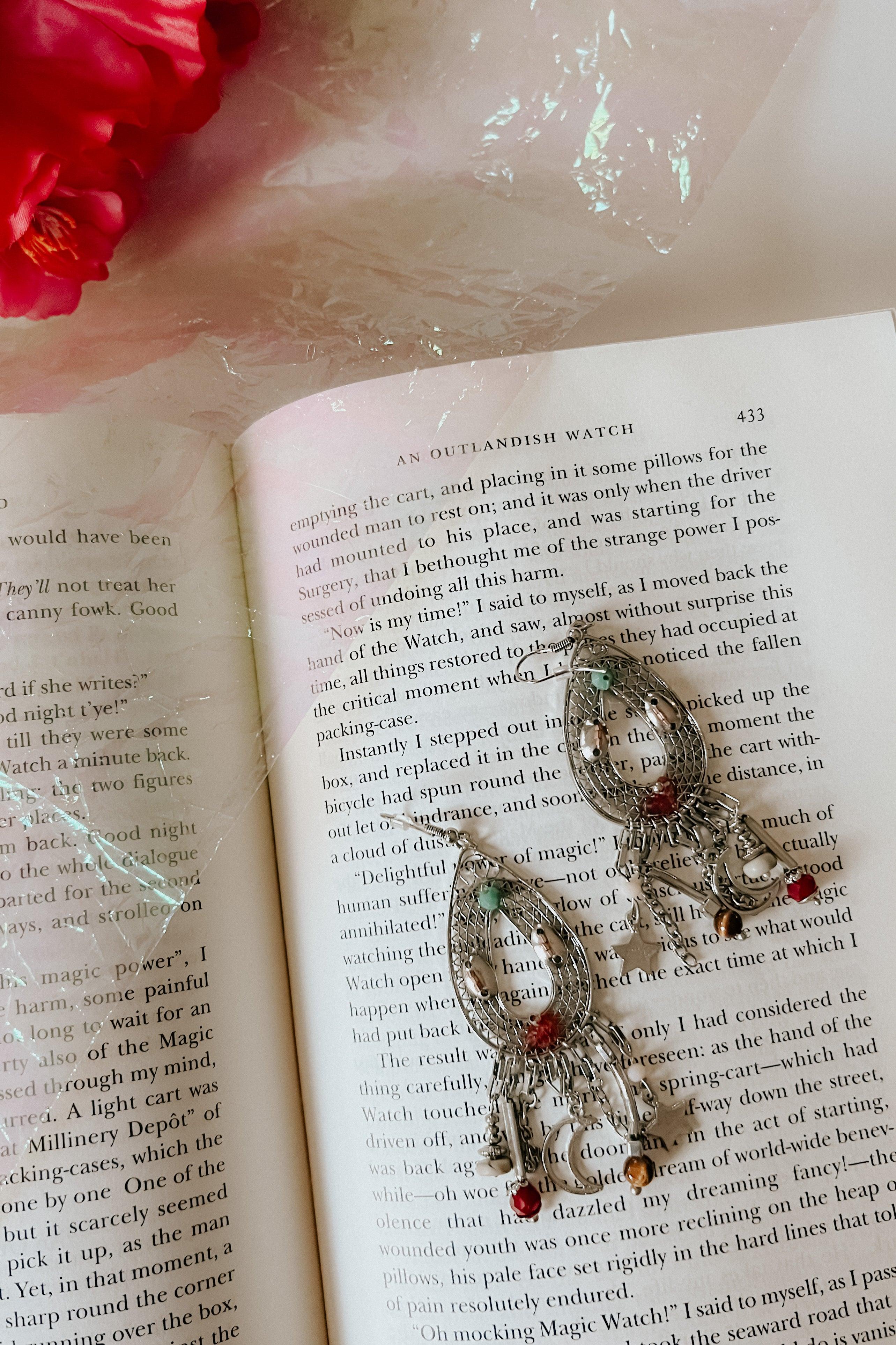 Silver teardrop earrings with colorful beads and dangling charms resting on an open book page