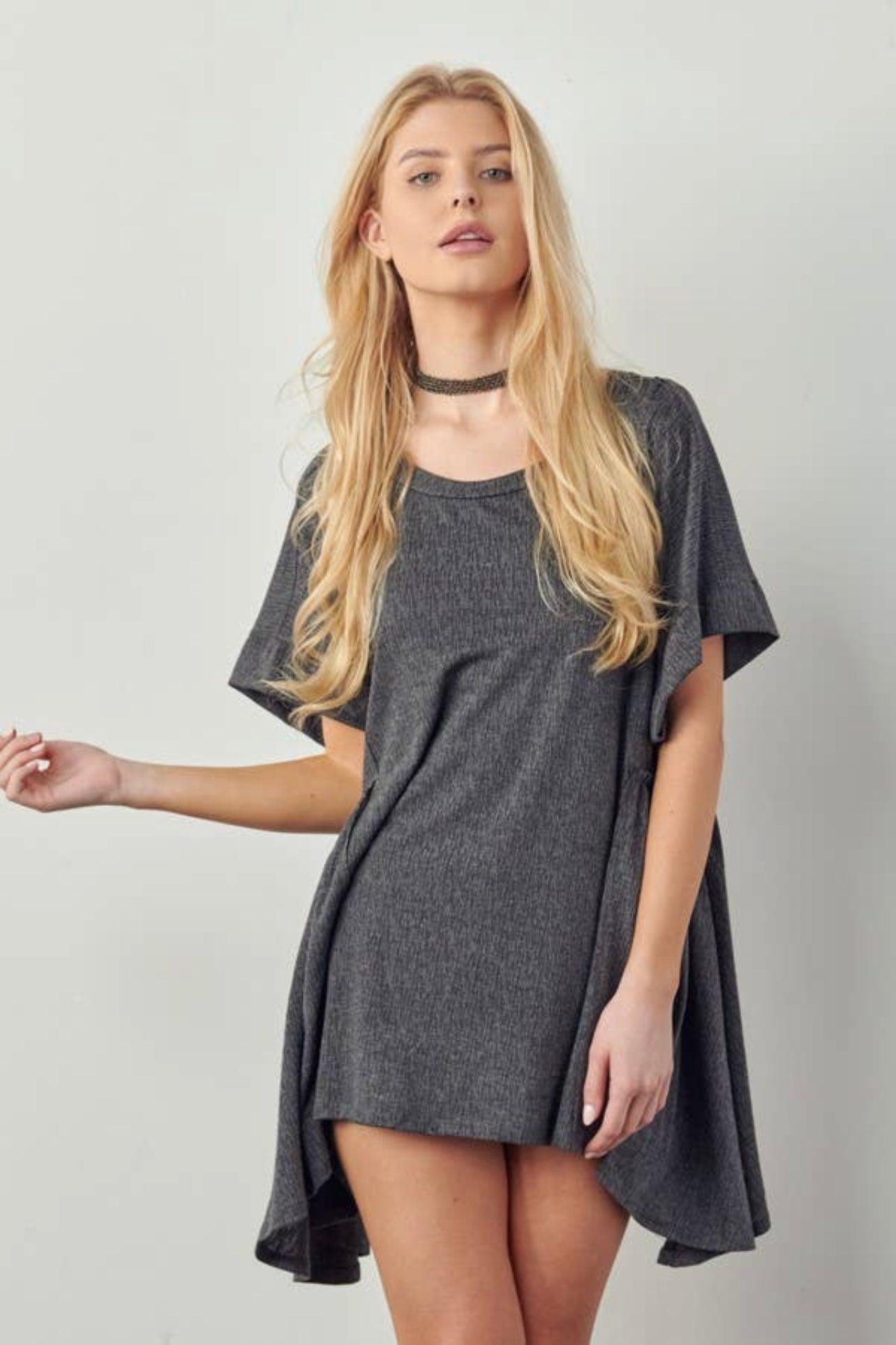 Blonde model wearing a loose dark gray oversized tunic dress with short sleeves and draped hem against plain background