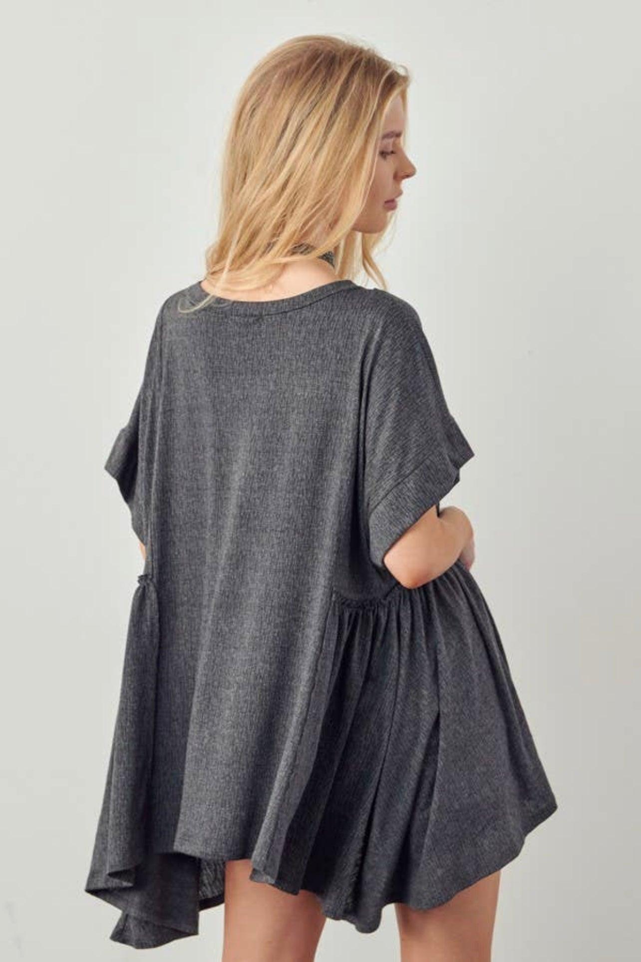 Blonde woman wearing loose dark gray oversized tunic with short sleeves and gathered side detail facing sideways