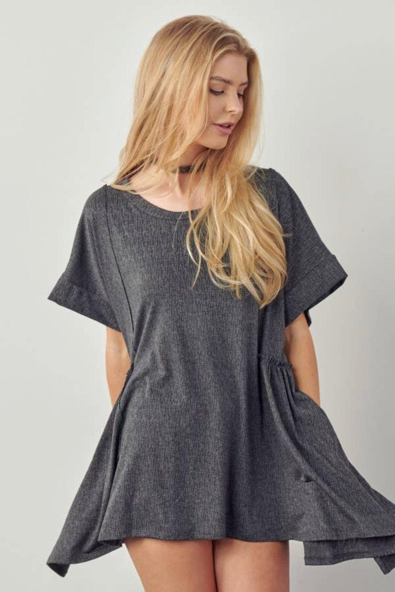 Blonde woman wearing loose charcoal gray oversized tunic dress with short sleeves and shark bite hem