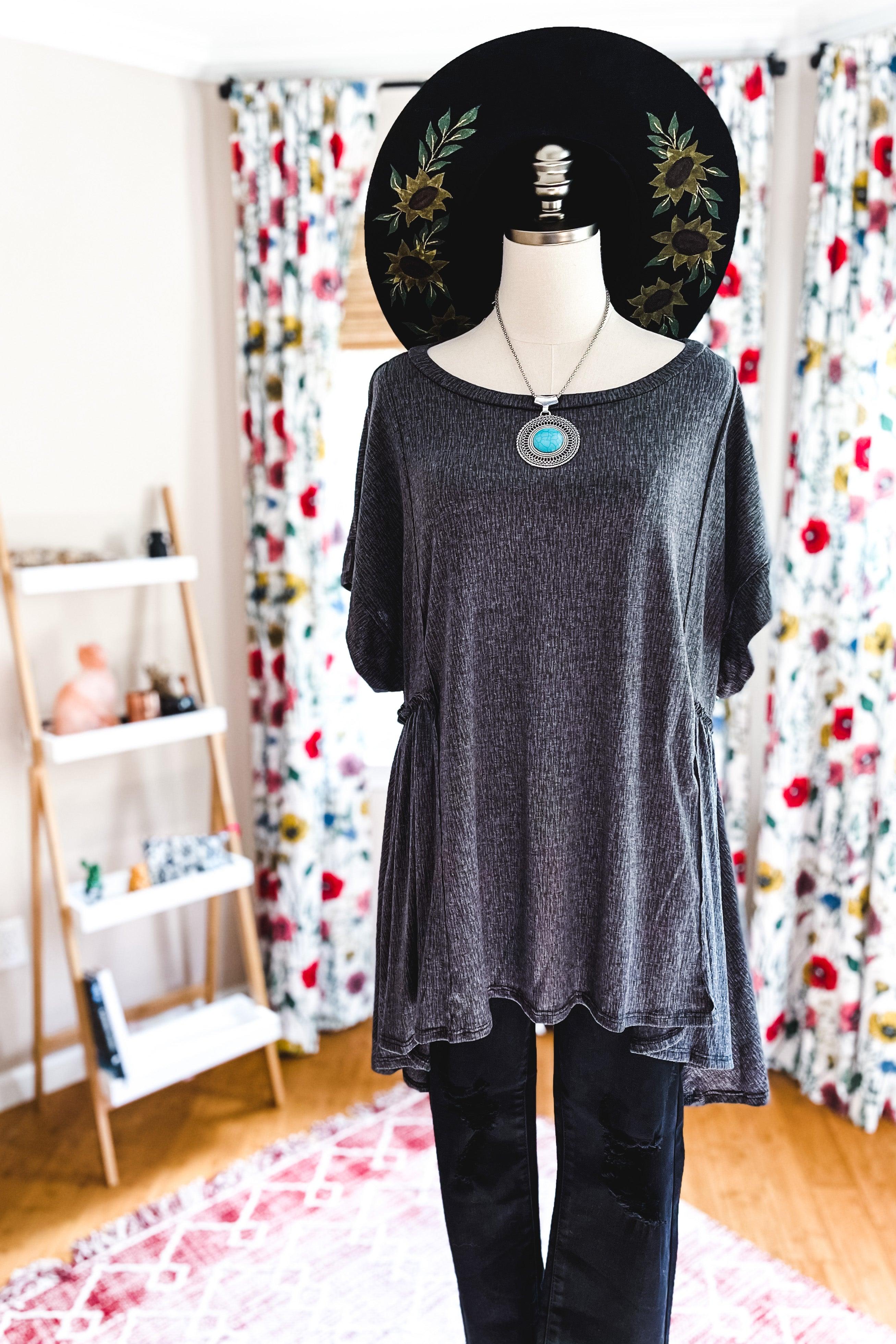 Mannequin dressed in dark gray oversized tunic with wide short sleeves and flowy hem paired with black pants and hat