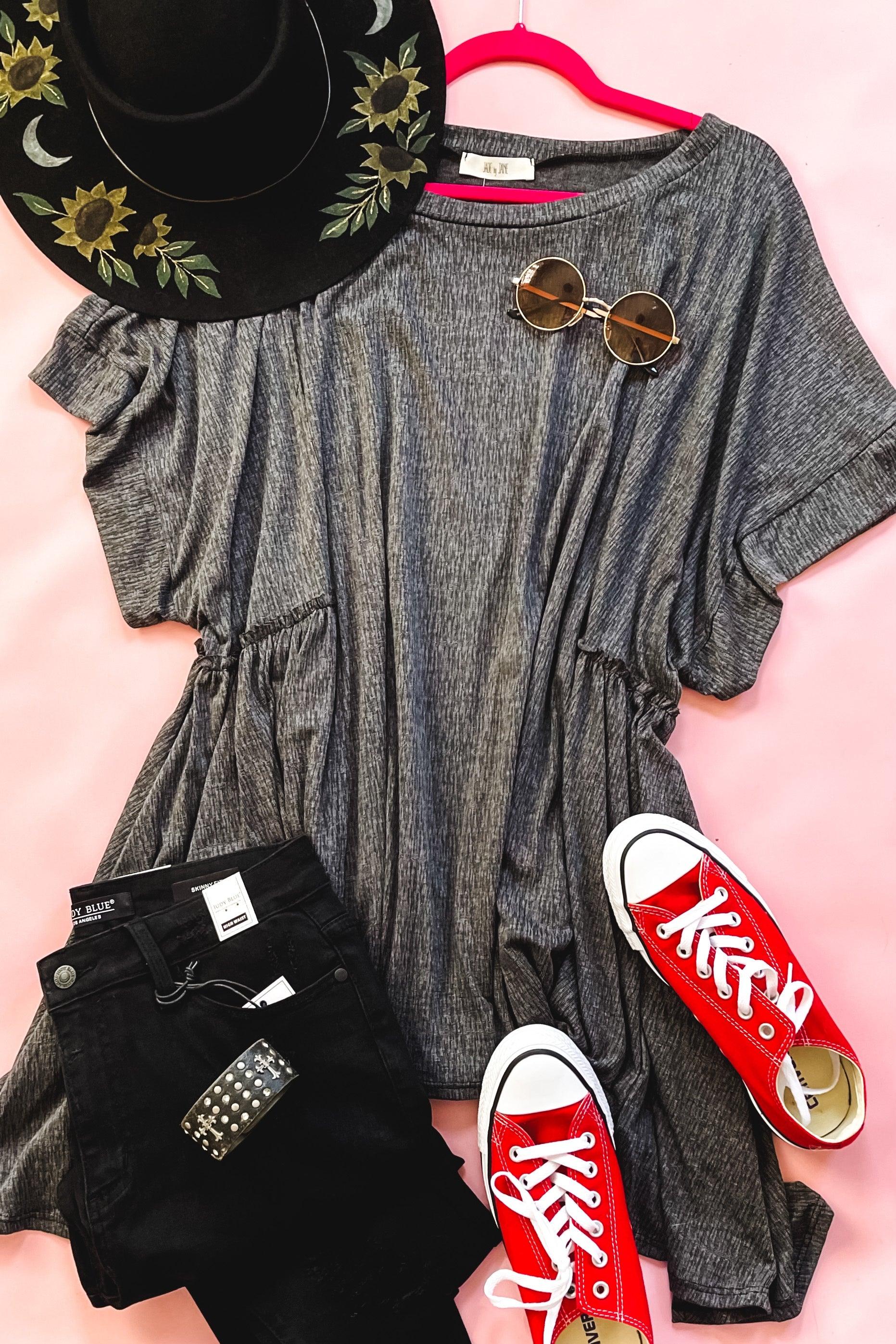 Gray oversized shark bite tunic with sunglasses, black embroidered hat, black jeans, and red canvas sneakers on pink background