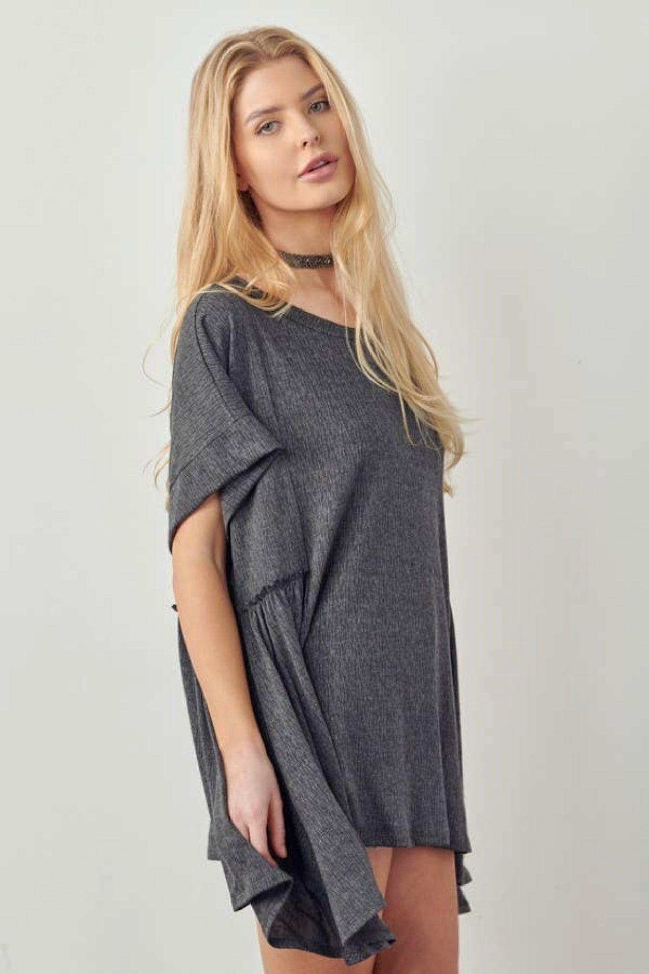 Blonde woman wearing loose dark gray oversized tunic with short sleeves and subtle gathered side detail against plain background
