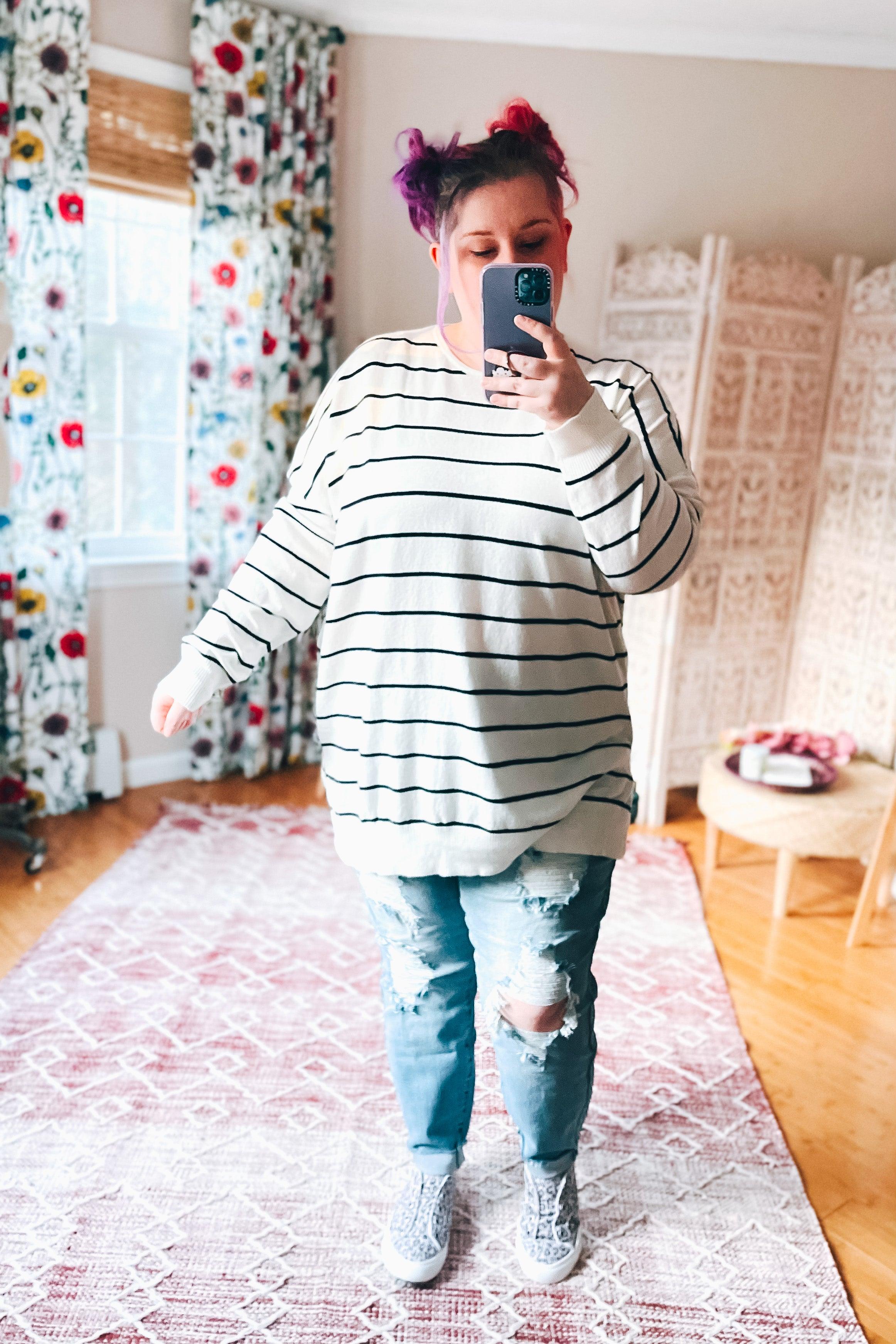 Person wearing purple gray water leopard slip-on sneakers with ripped light blue jeans and striped long sleeve top indoors