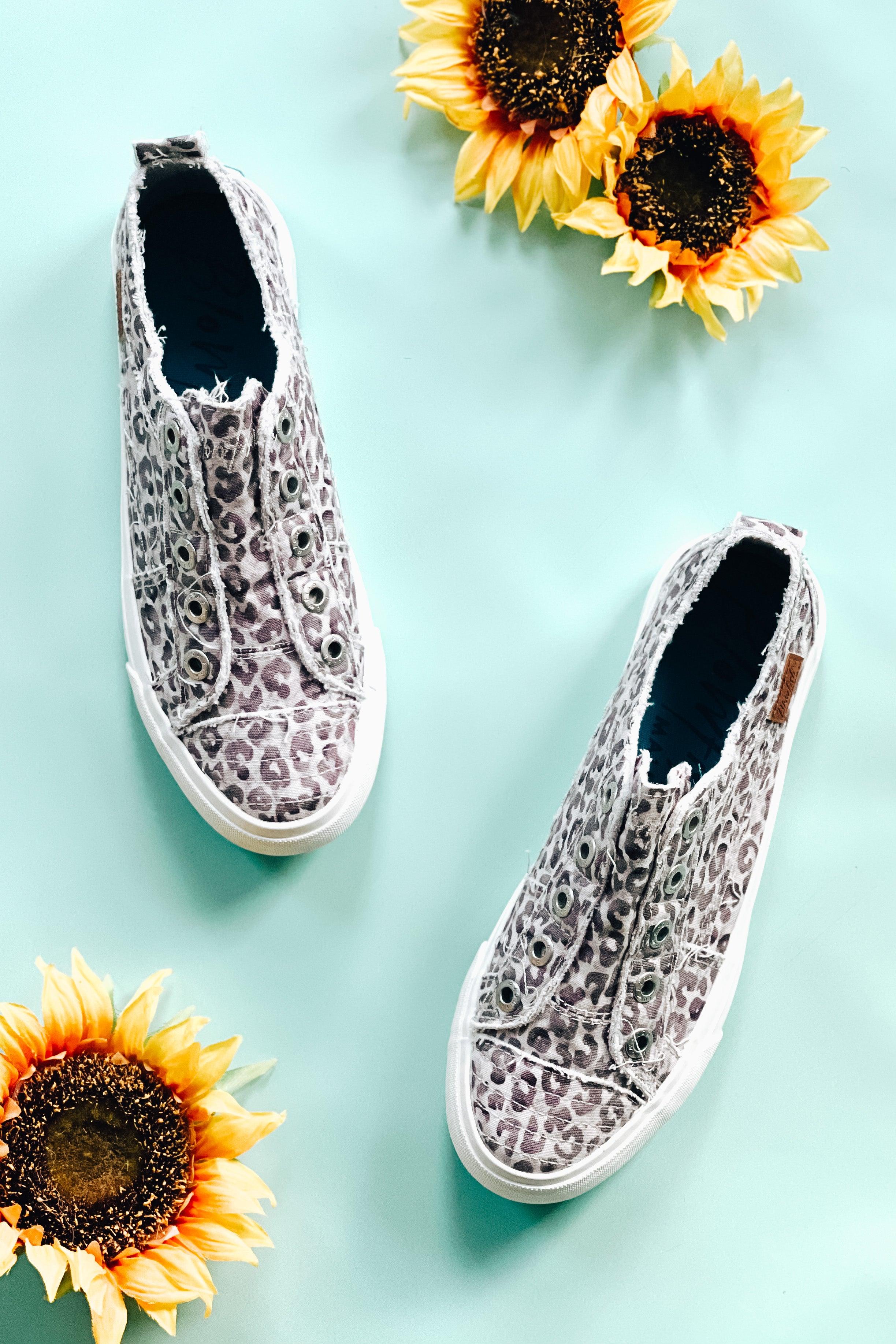 Frayed edge purple gray water leopard print slip-on sneakers displayed on pale blue surface with sunflowers