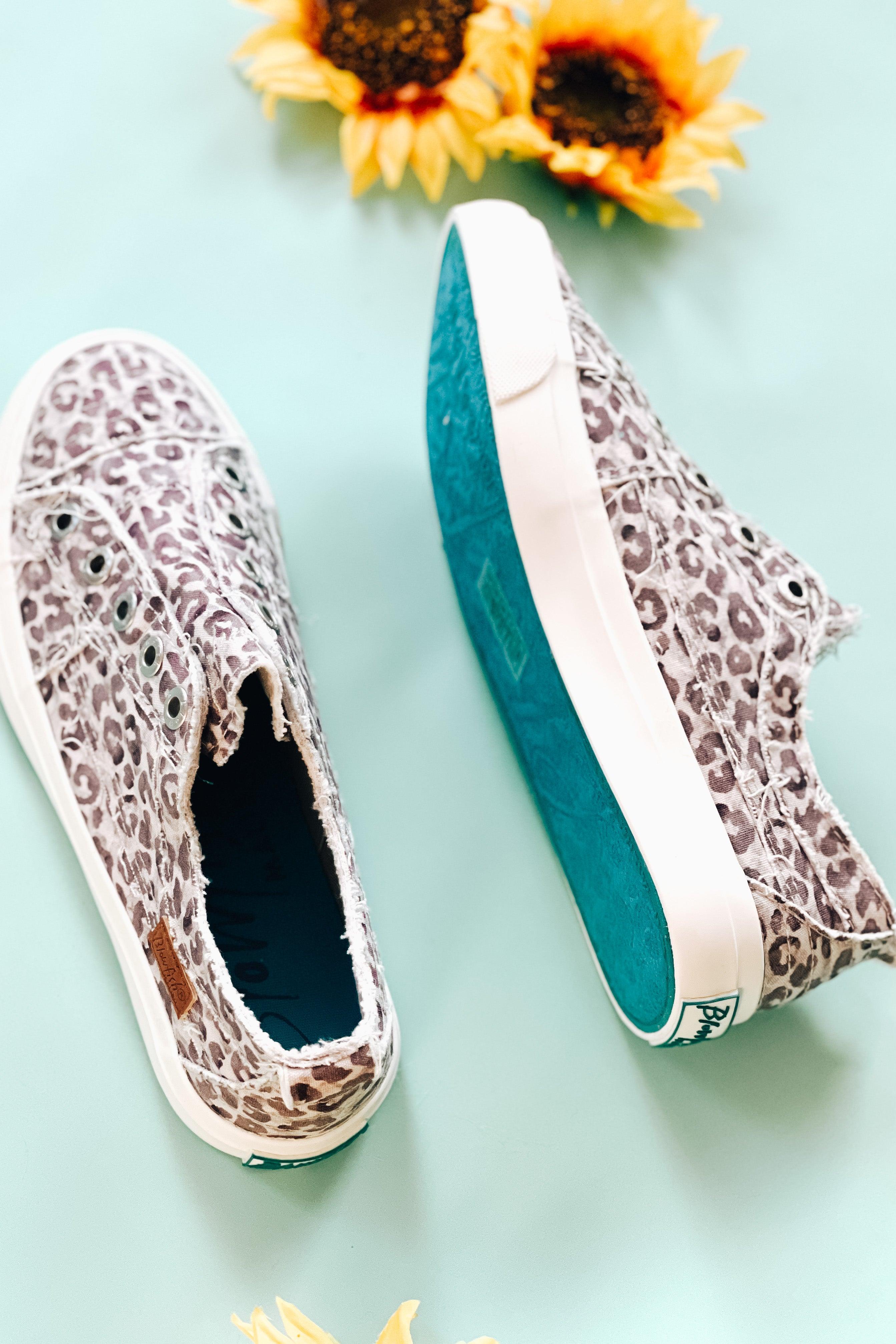 Purple gray water leopard print slip-on sneakers with teal rubber sole displayed beside sunflowers on pale blue surface