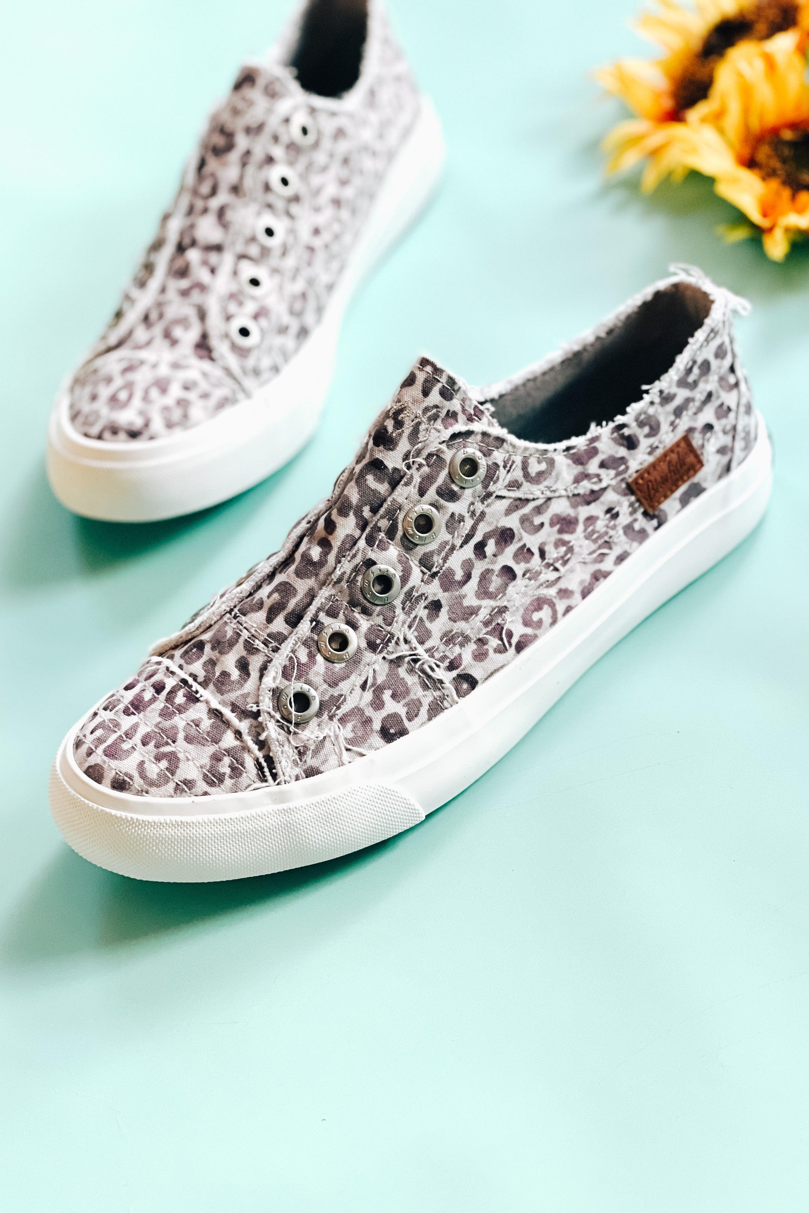 Slip-on canvas sneakers in purple gray water leopard print with white soles on light blue background beside sunflowers