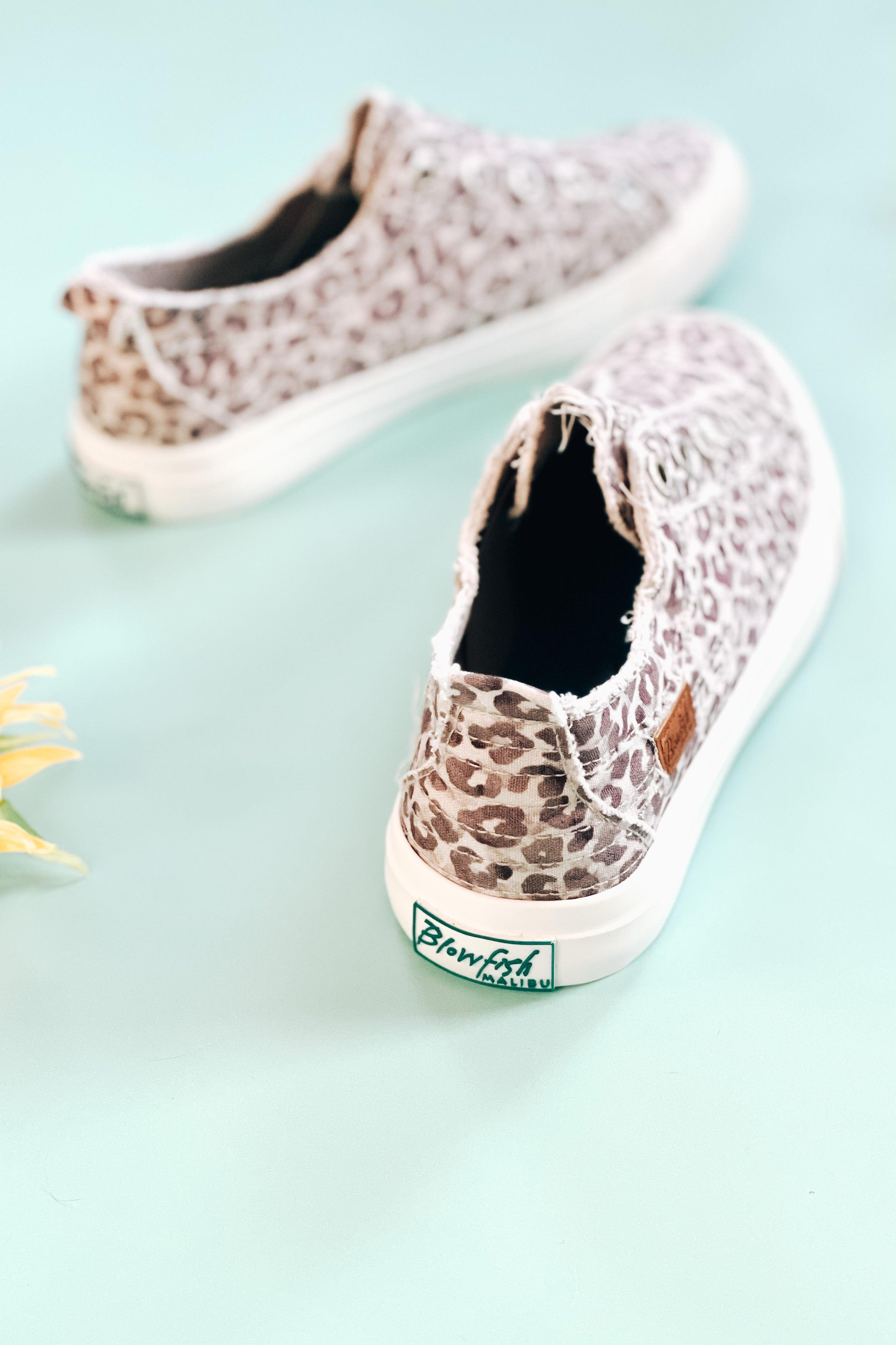 Pair of purple gray water leopard print canvas slip-on sneakers on light blue surface with flower nearby