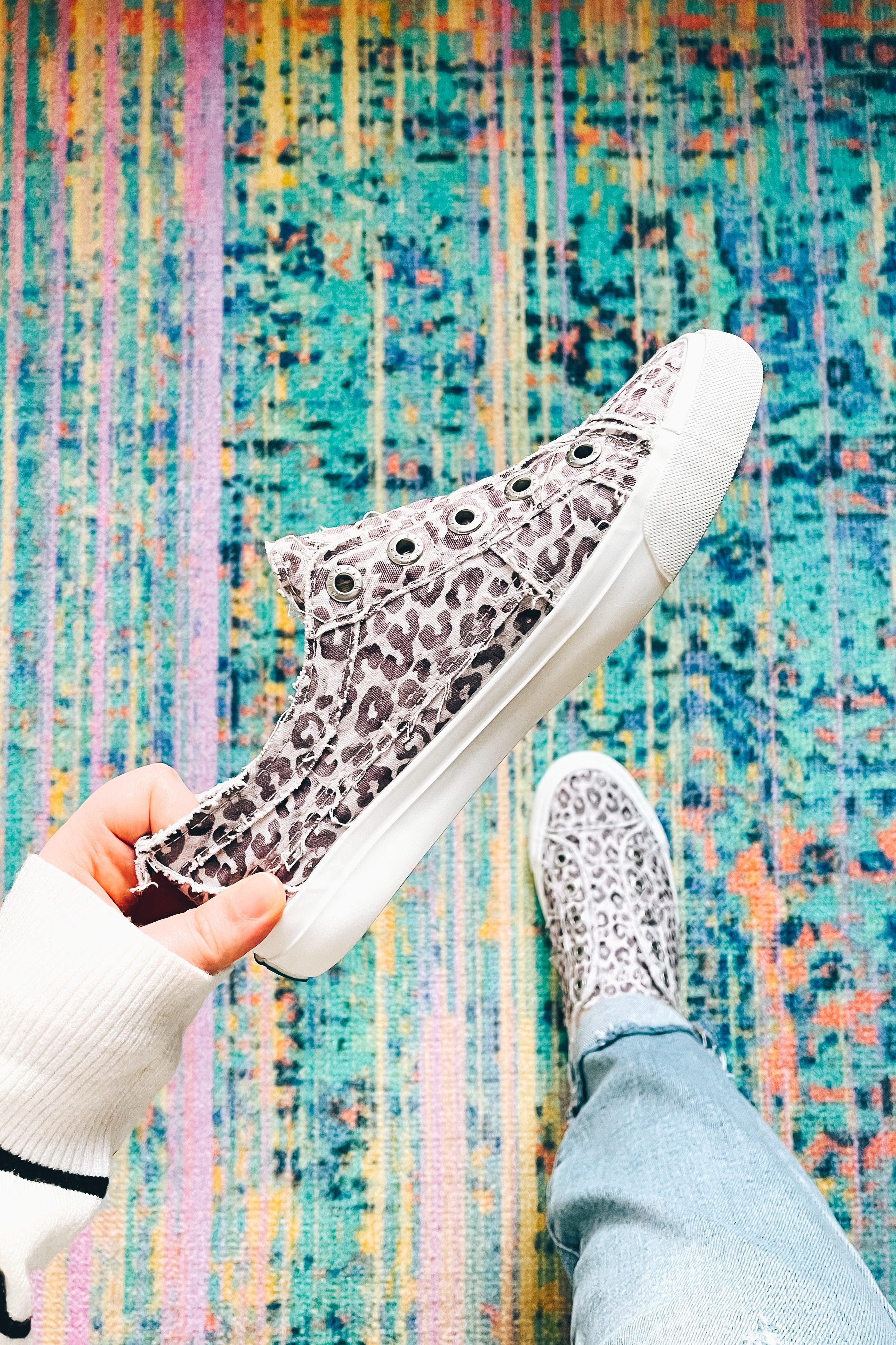 Hand holding purple gray leopard print canvas sneaker above colorful textured rug with person wearing matching shoe