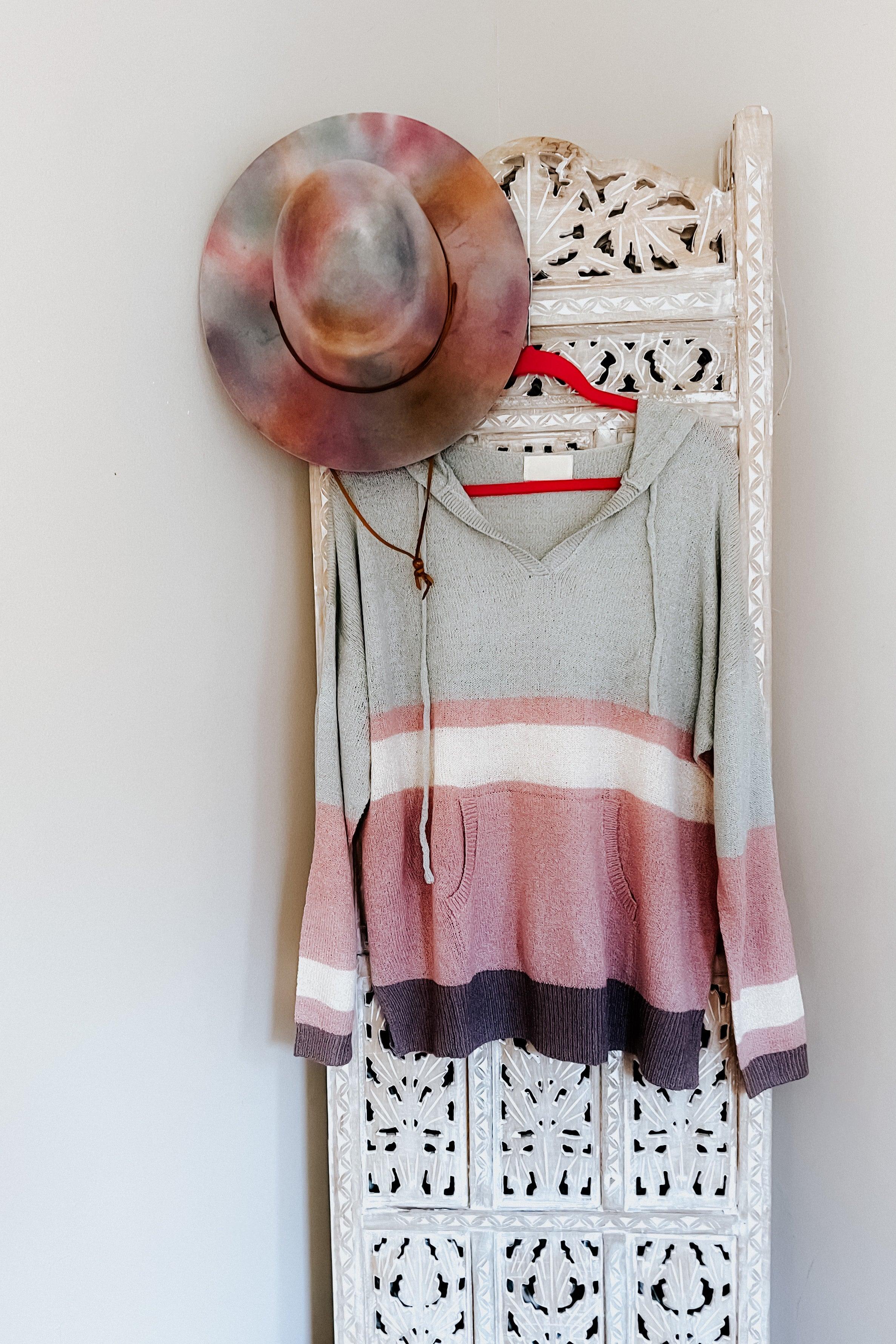 Boy Problem Spring Hoodie with muted pastel stripes hanging on decorative white carved panel with tie-dye hat