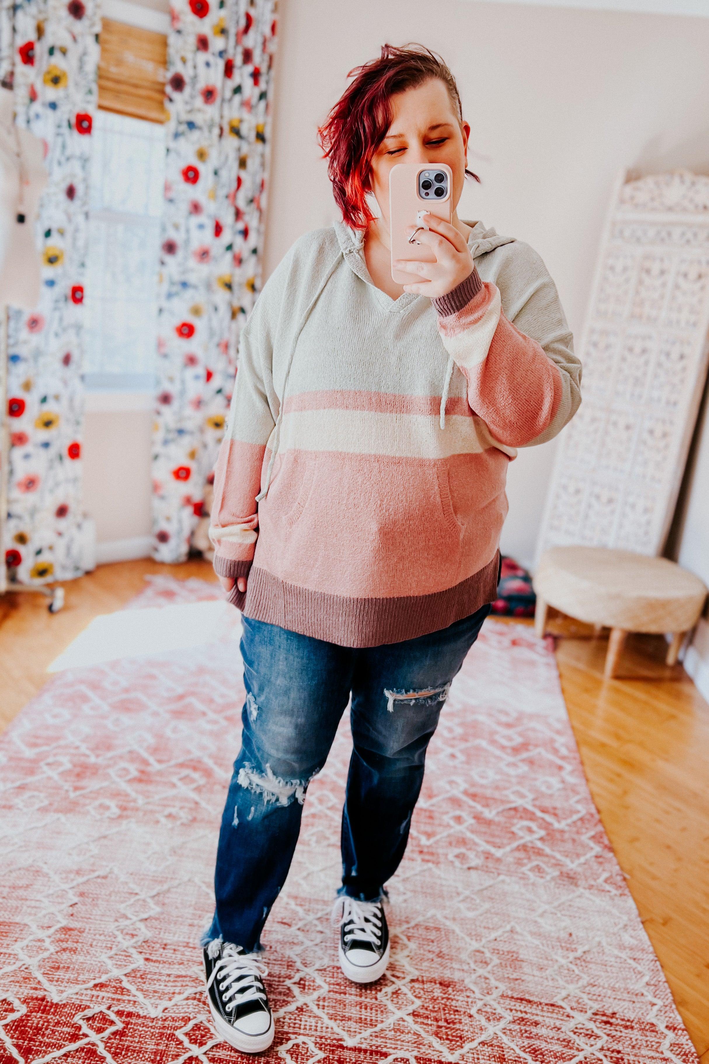 Woman wearing pastel striped Boy Problem Spring Hoodie and ripped jeans taking selfie in bright room with floral curtains