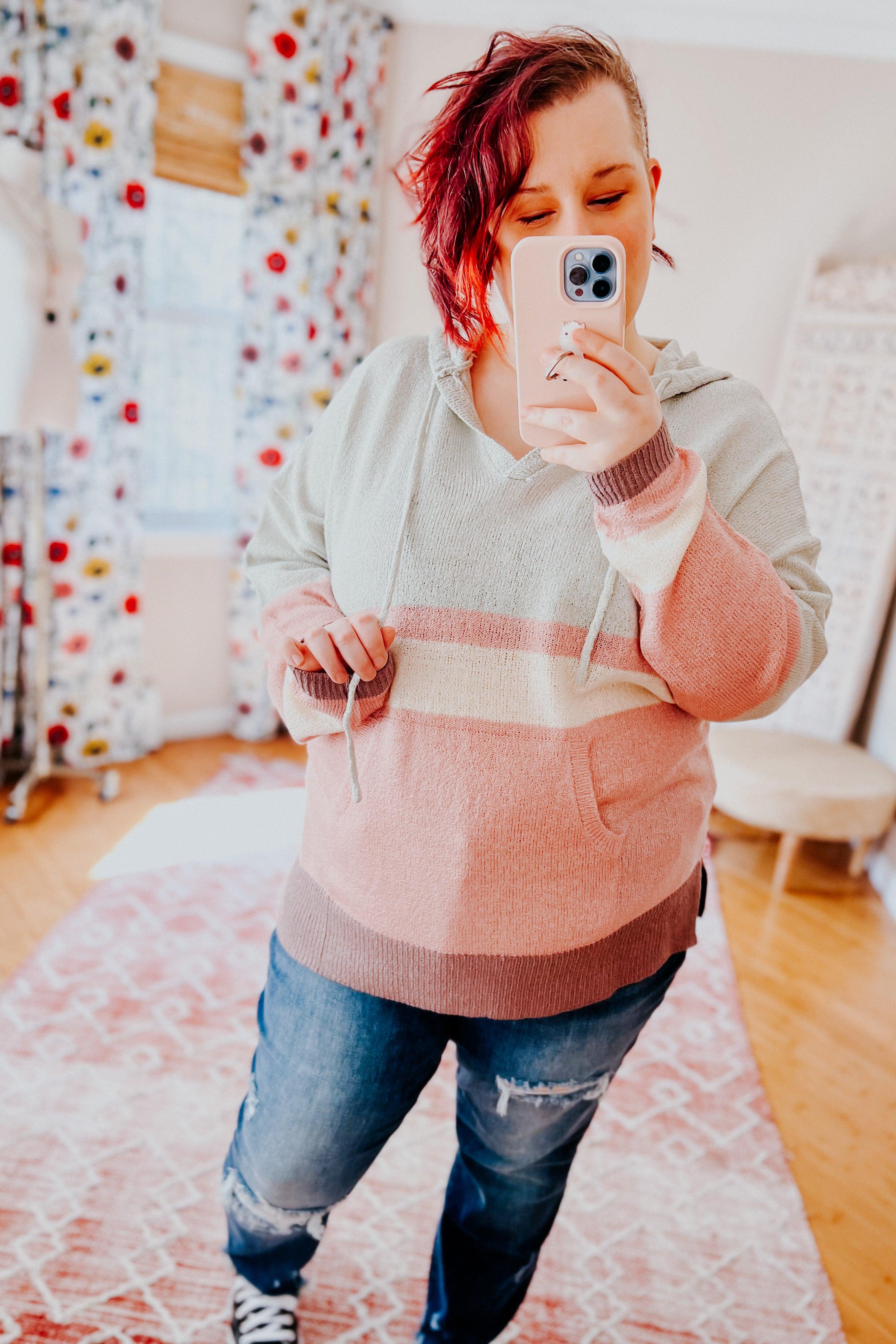 Woman with short red hair wearing pastel color-blocked Boy Problem Spring Hoodie and ripped jeans taking a selfie indoors