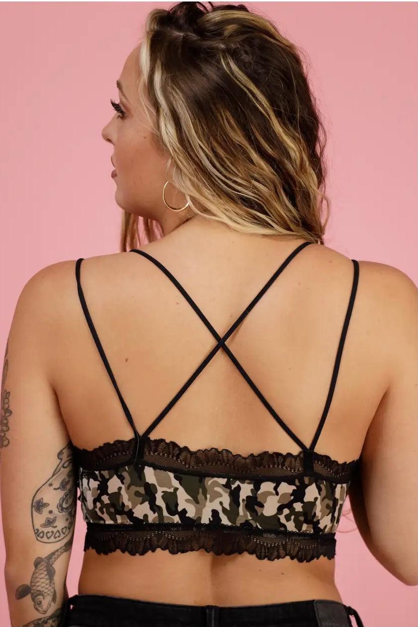 Back view of camo bralette with black lace trim and crossed thin straps worn by tattooed woman against pink background