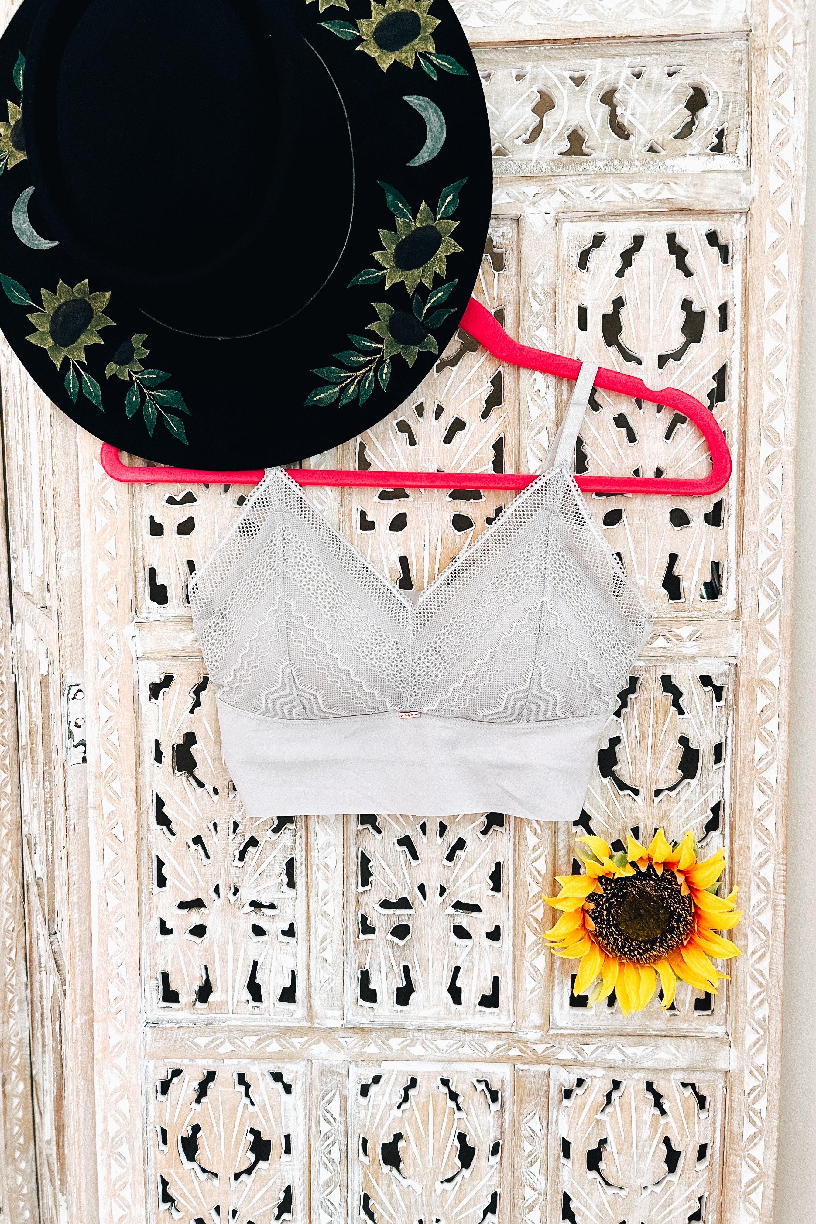 Silver lace bralette hanging on bright pink hanger with black floral hat and sunflower on carved wooden door background