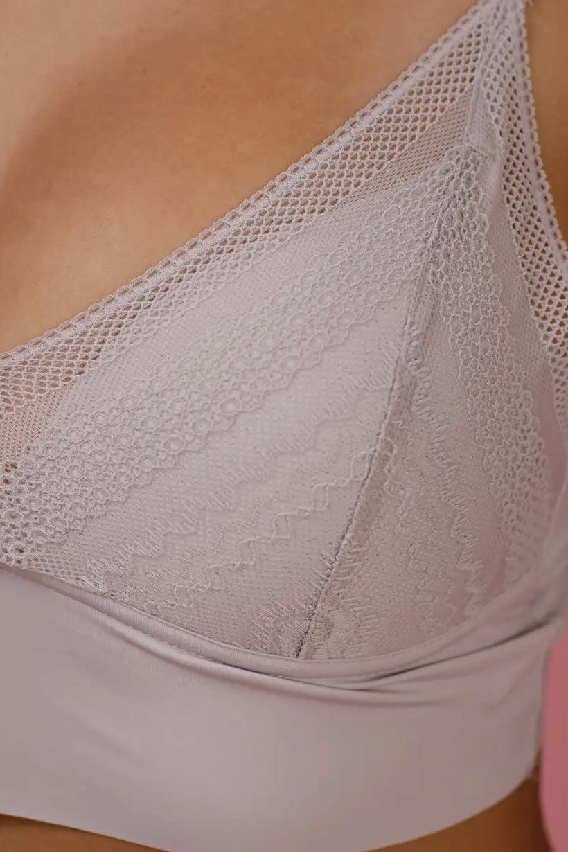 Close-up of silver lace bralette fabric with delicate floral and geometric patterns on soft skin background