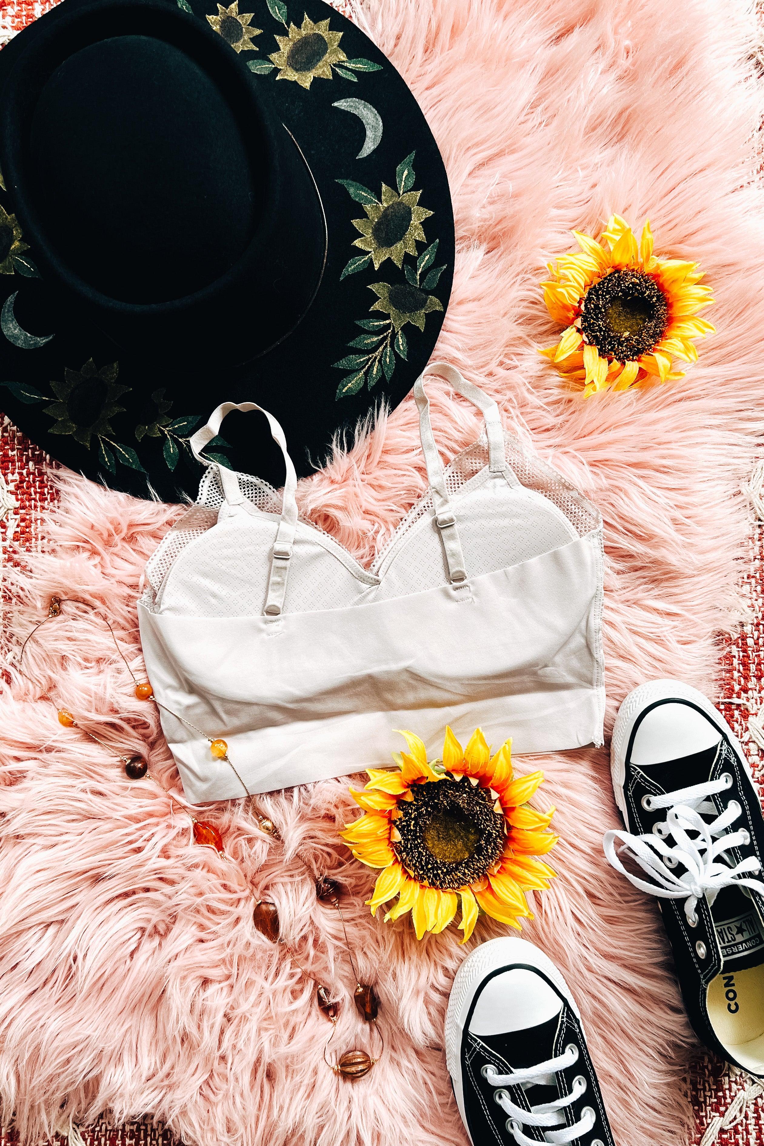 Silver lace-trimmed bralette styled on pink faux fur with black floral hat, sunflower accents, and black sneakers