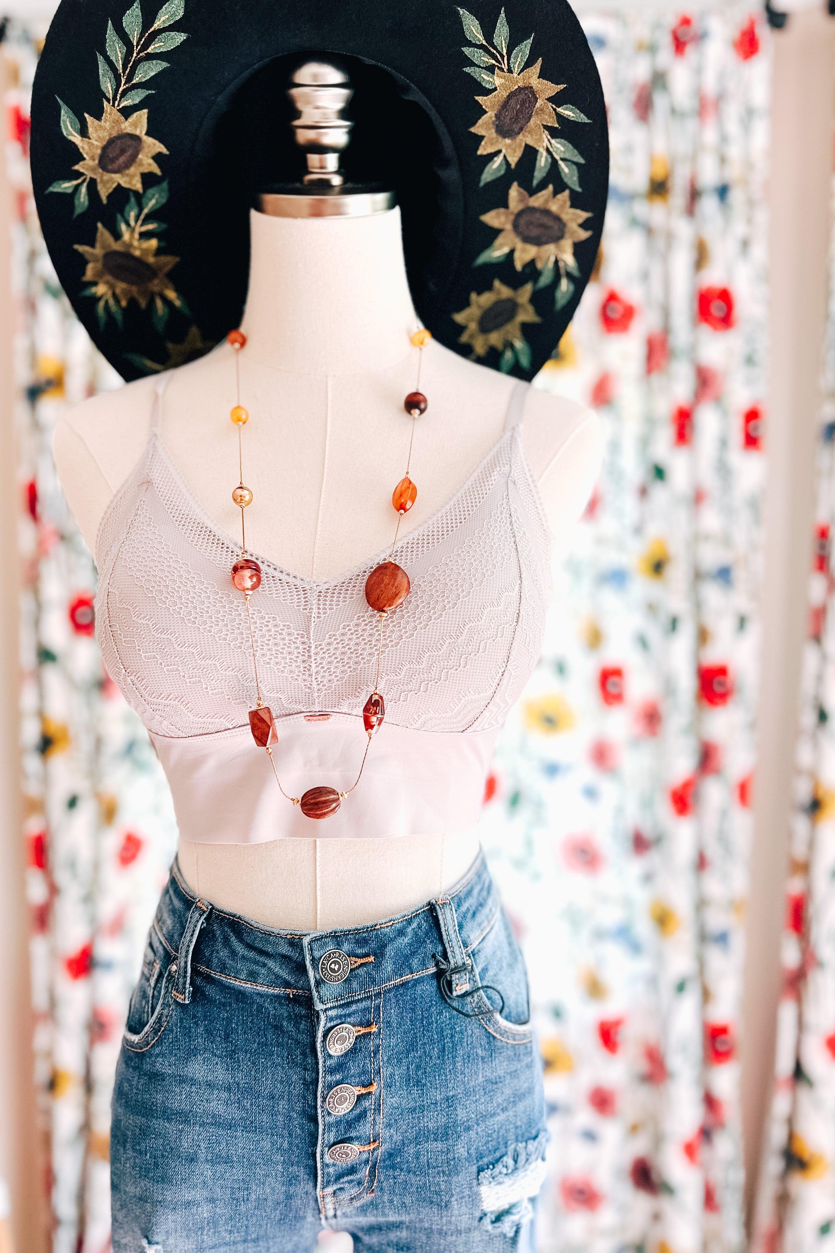 Mannequin dressed in silver lace bralette, layered necklace, distressed button-fly denim skirt, and black wide-brim floral hat