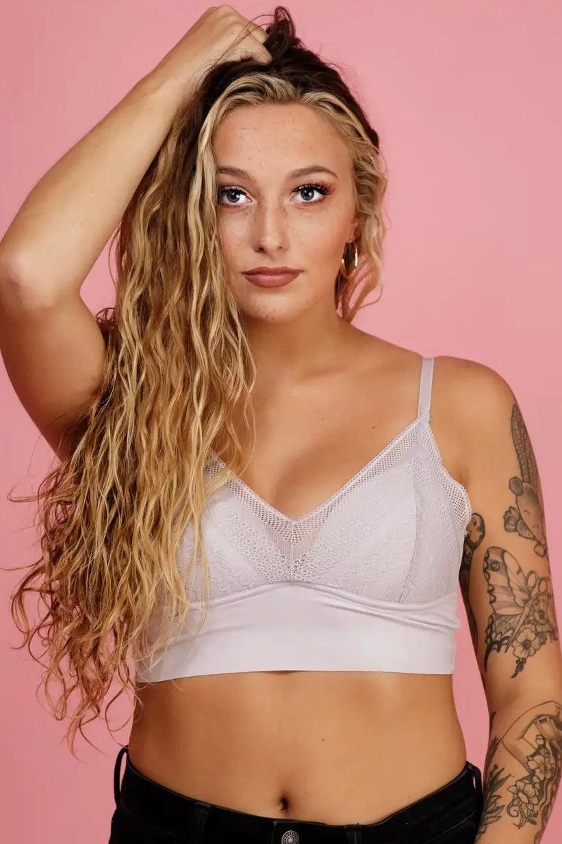 Front view of woman with long wavy hair wearing a silver lace Daydream Baby Bralette against pink backdrop