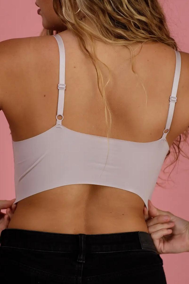 Back view of woman wearing smooth silver bralette with adjustable straps against pink background