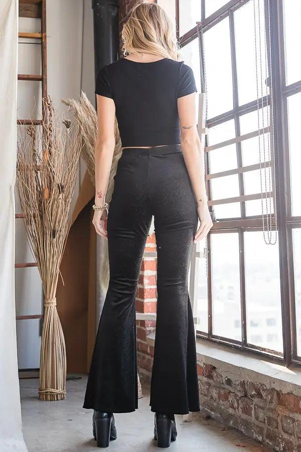 Woman wearing black glittery bell bottoms and black fitted short sleeve top standing indoors near window
