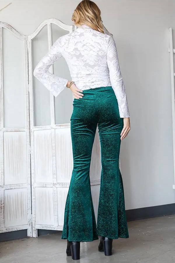 Back view of woman wearing emerald green glitter velvet bell bottoms with black platform boots indoors