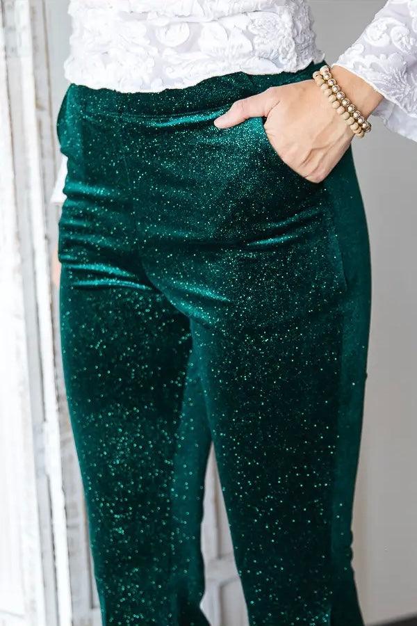 Close-up of glittery emerald green velvet bell bottoms worn with white lace top and pearl bracelet on wrist