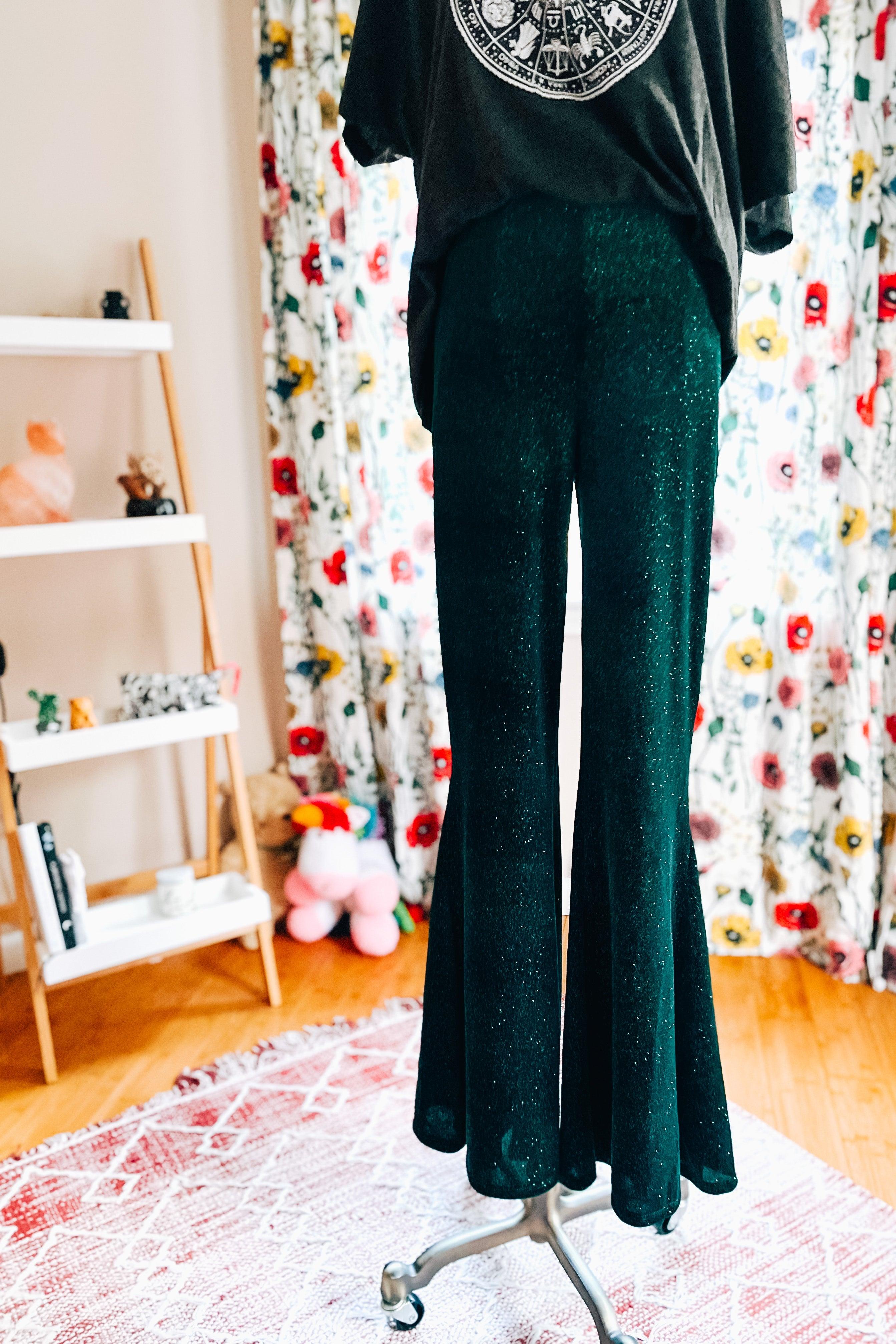 Evergreen glitter bell bottoms displayed on a mannequin in a cozy room with floral curtains and a patterned rug