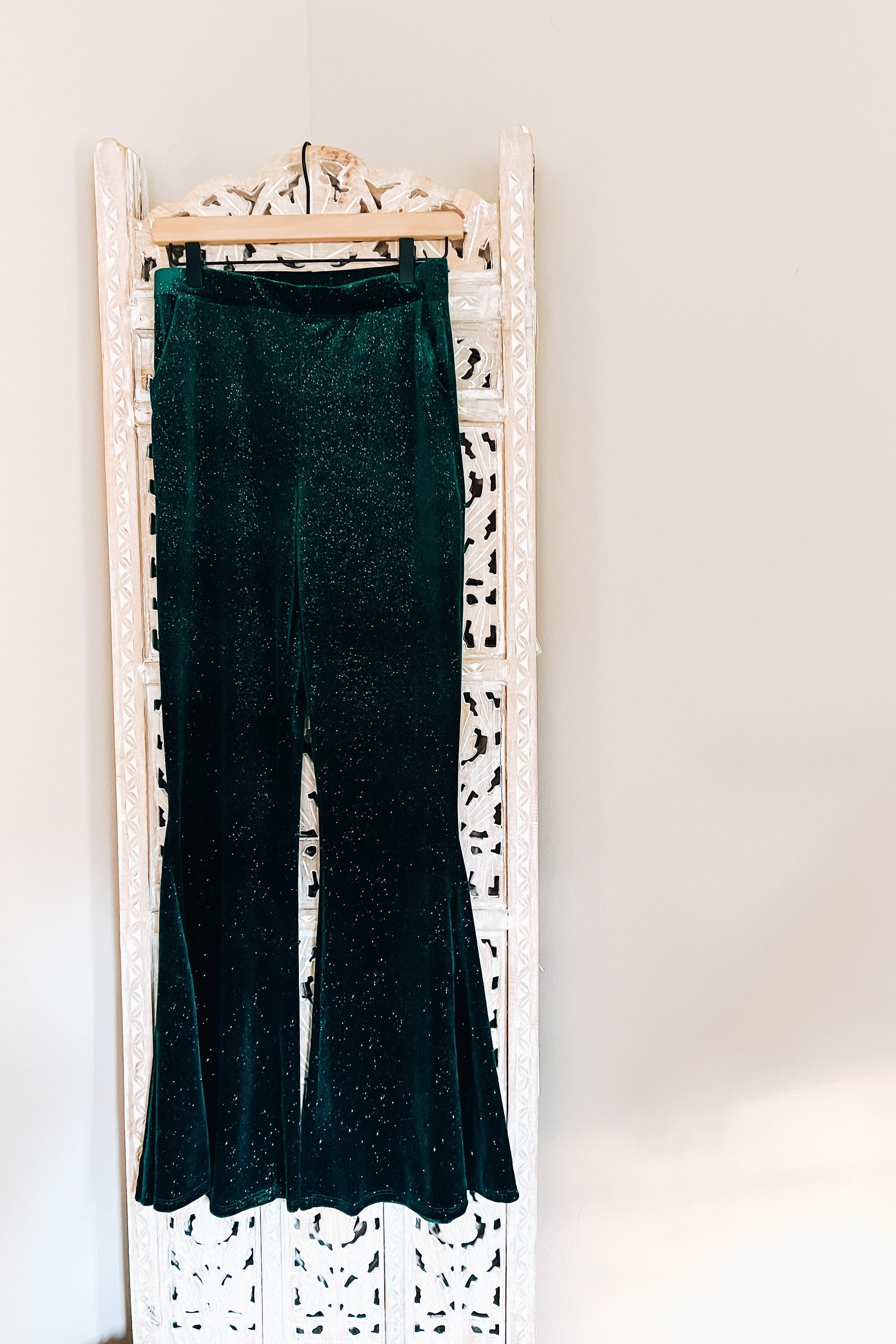 Evergreen velvet bell bottoms with glitter detail hanging on decorative carved wooden panel