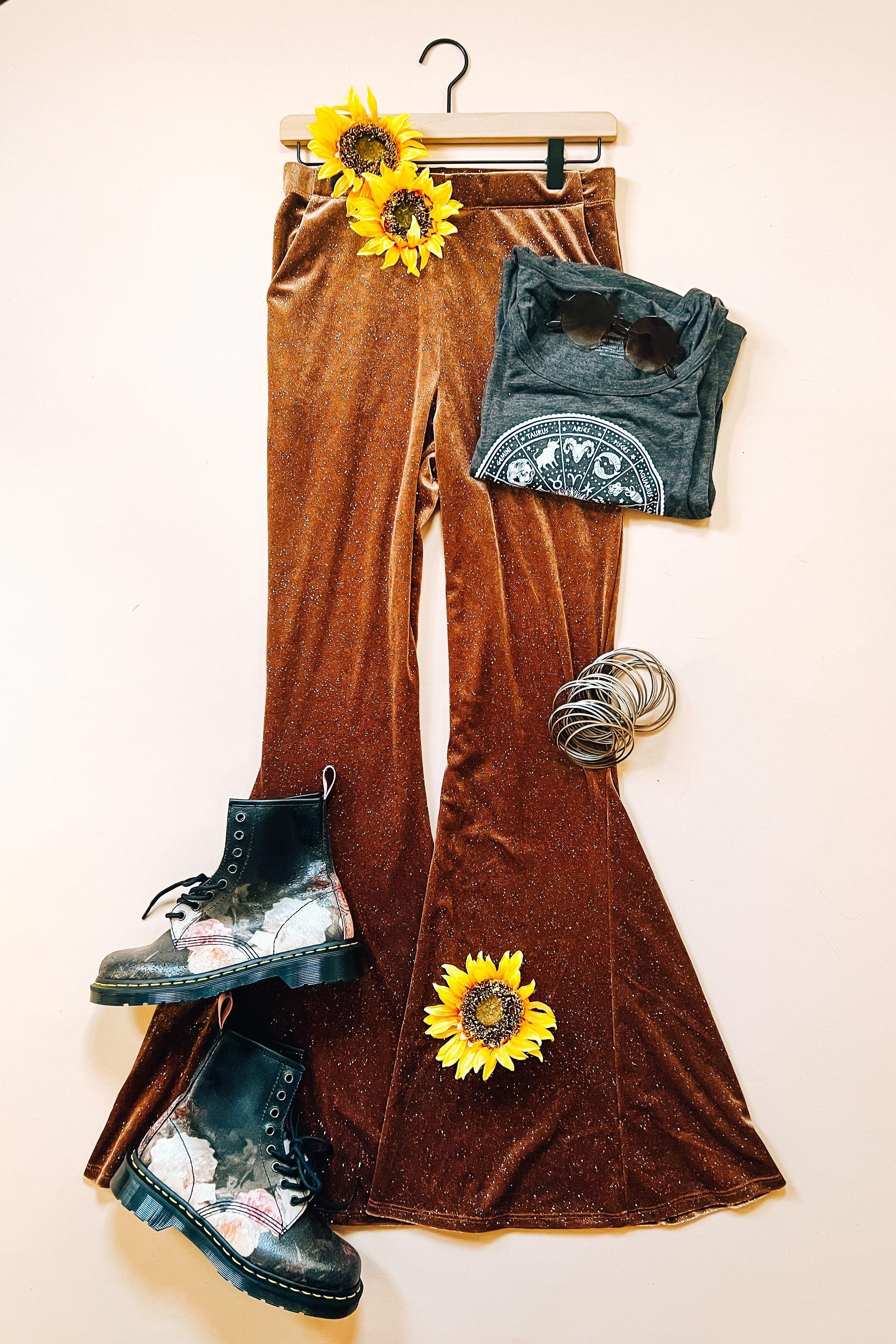 Brown glitter velvet bell bottoms styled with black floral combat boots, folded graphic tee, and silver bracelets with sunflowers on cream background