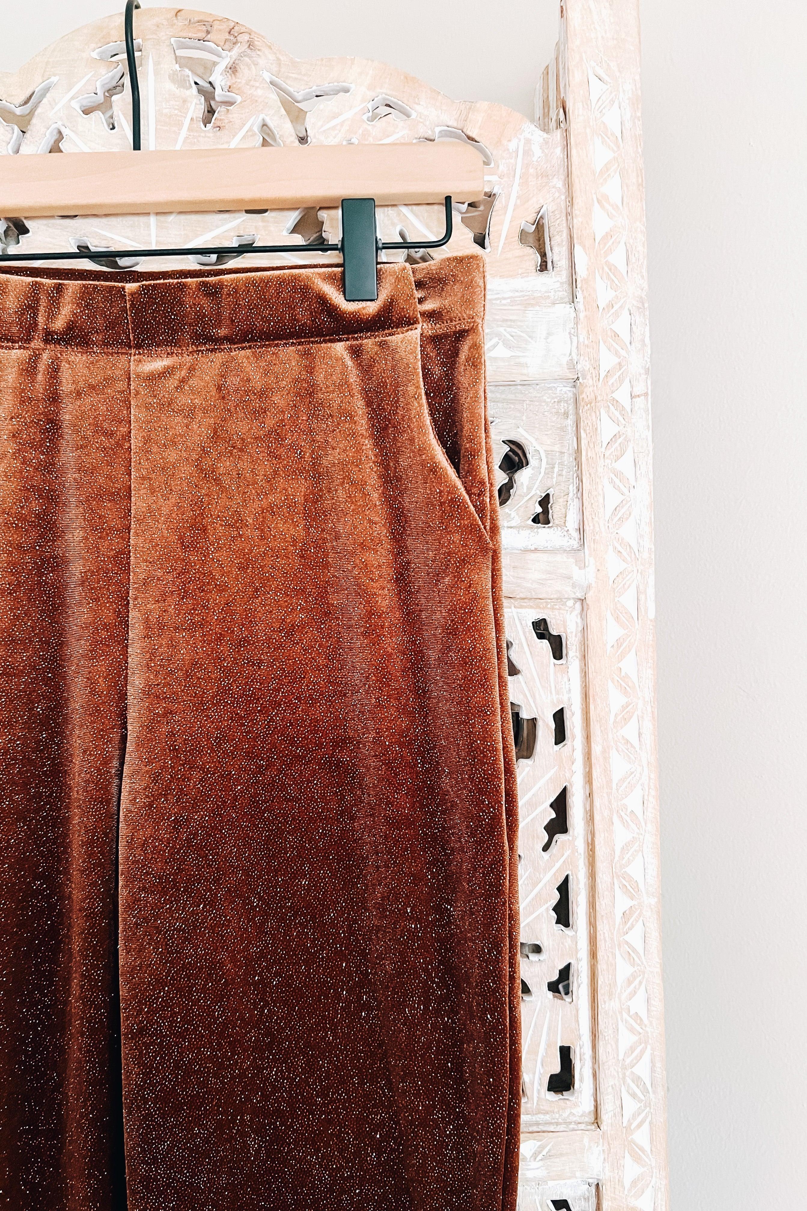 Close-up of gold glitter velvet bell bottoms hanging on wooden hanger against carved white panel background