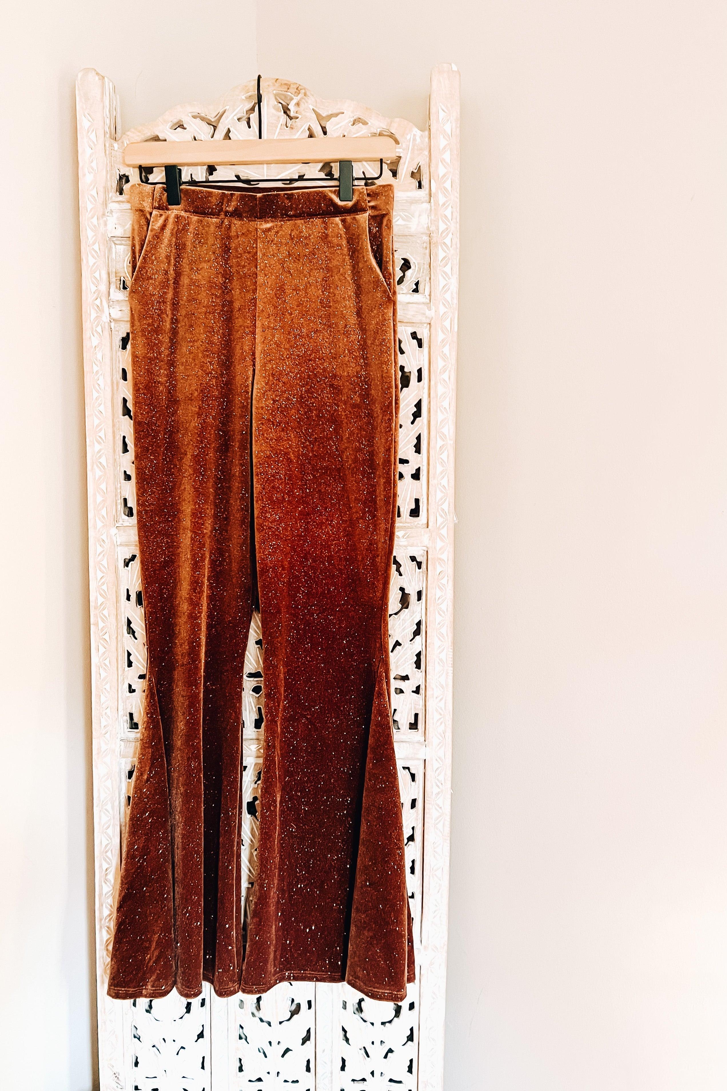 Gold velvet glitter bell bottoms hanging on wooden hanger in front of carved white decorative screen