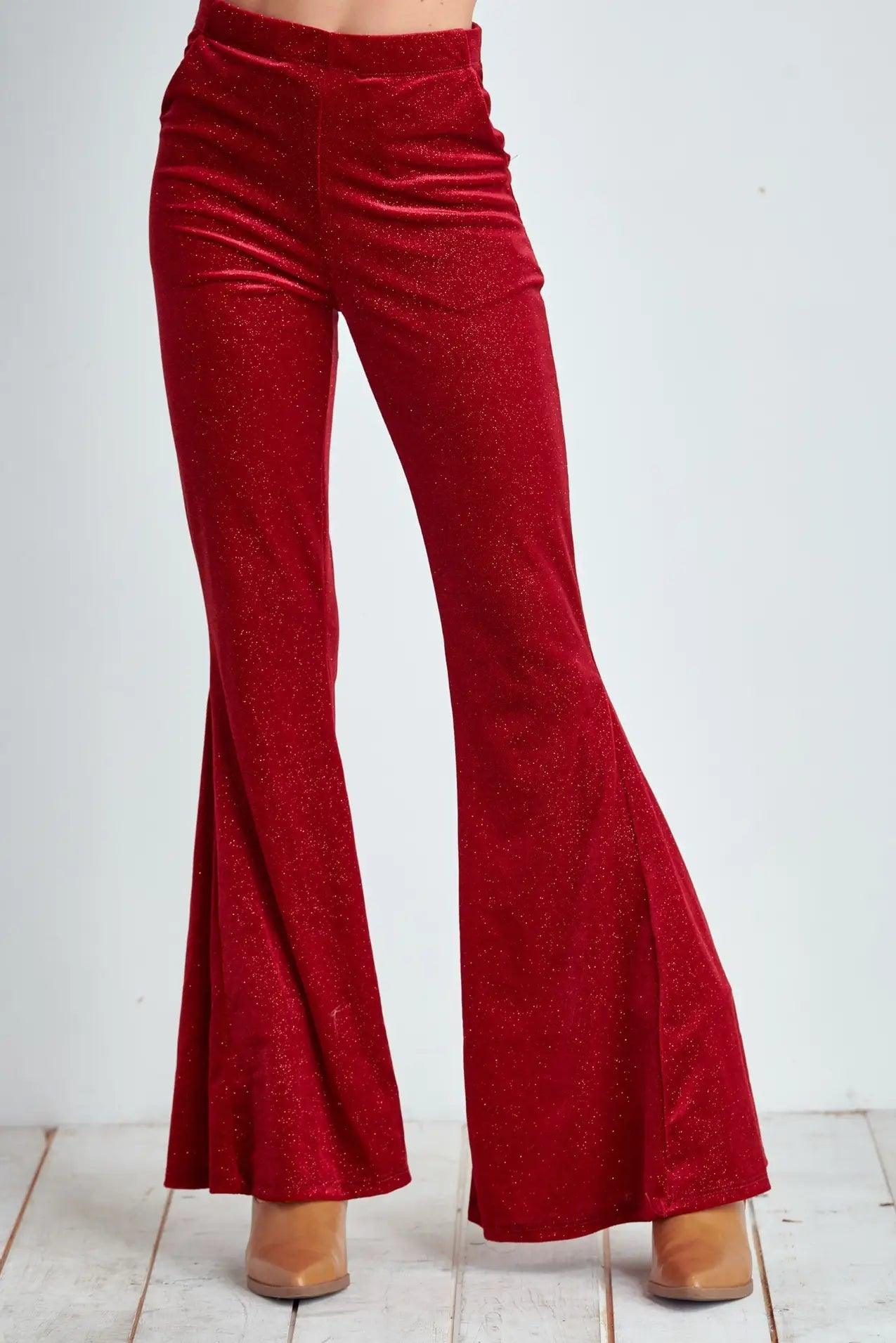 Front view of red velvet glitter bell bottoms with flare legs styled with tan boots on white floor