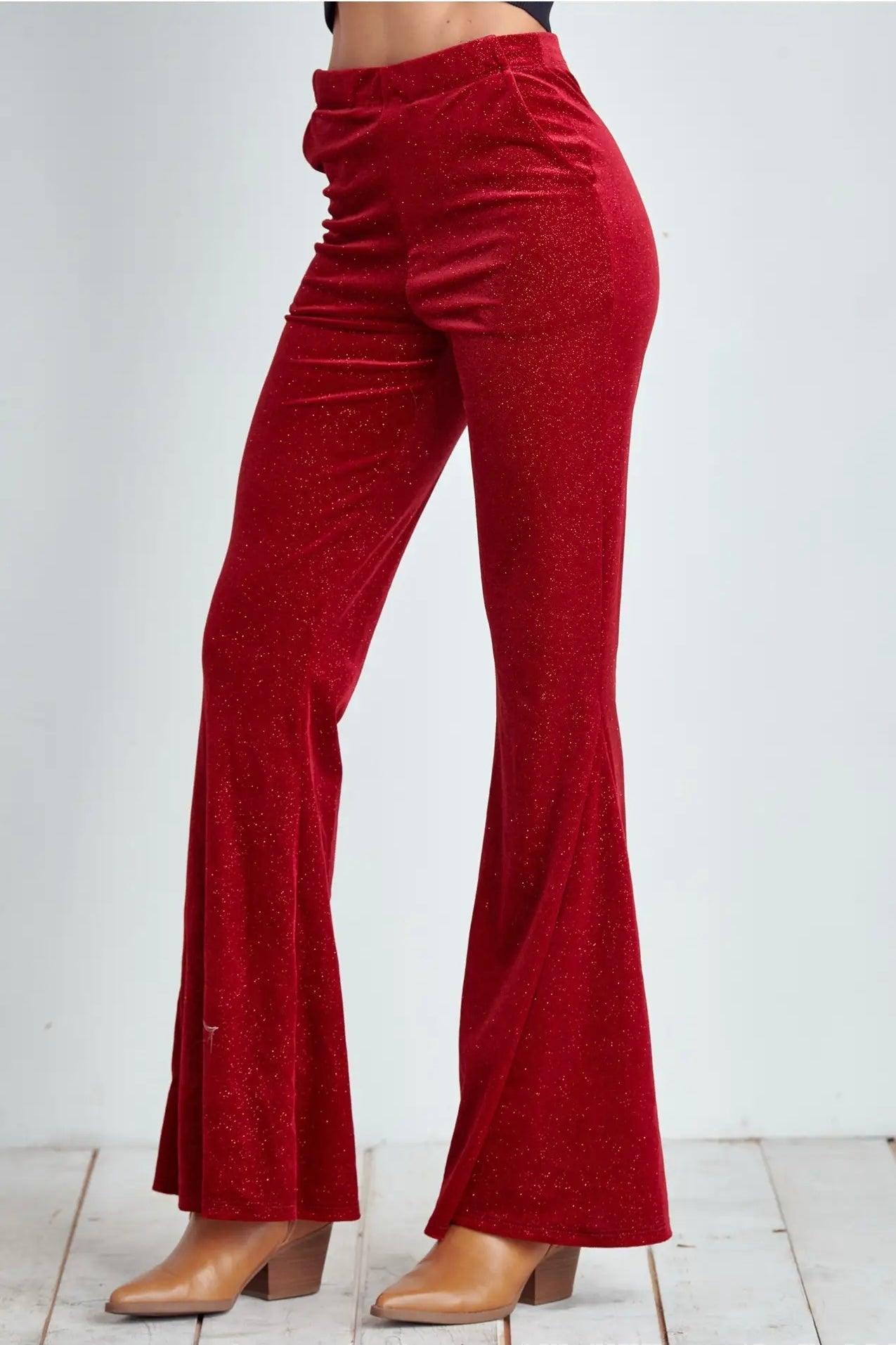 Close-up of ruby red glitter bell bottoms styled with tan heeled boots on white wooden floor