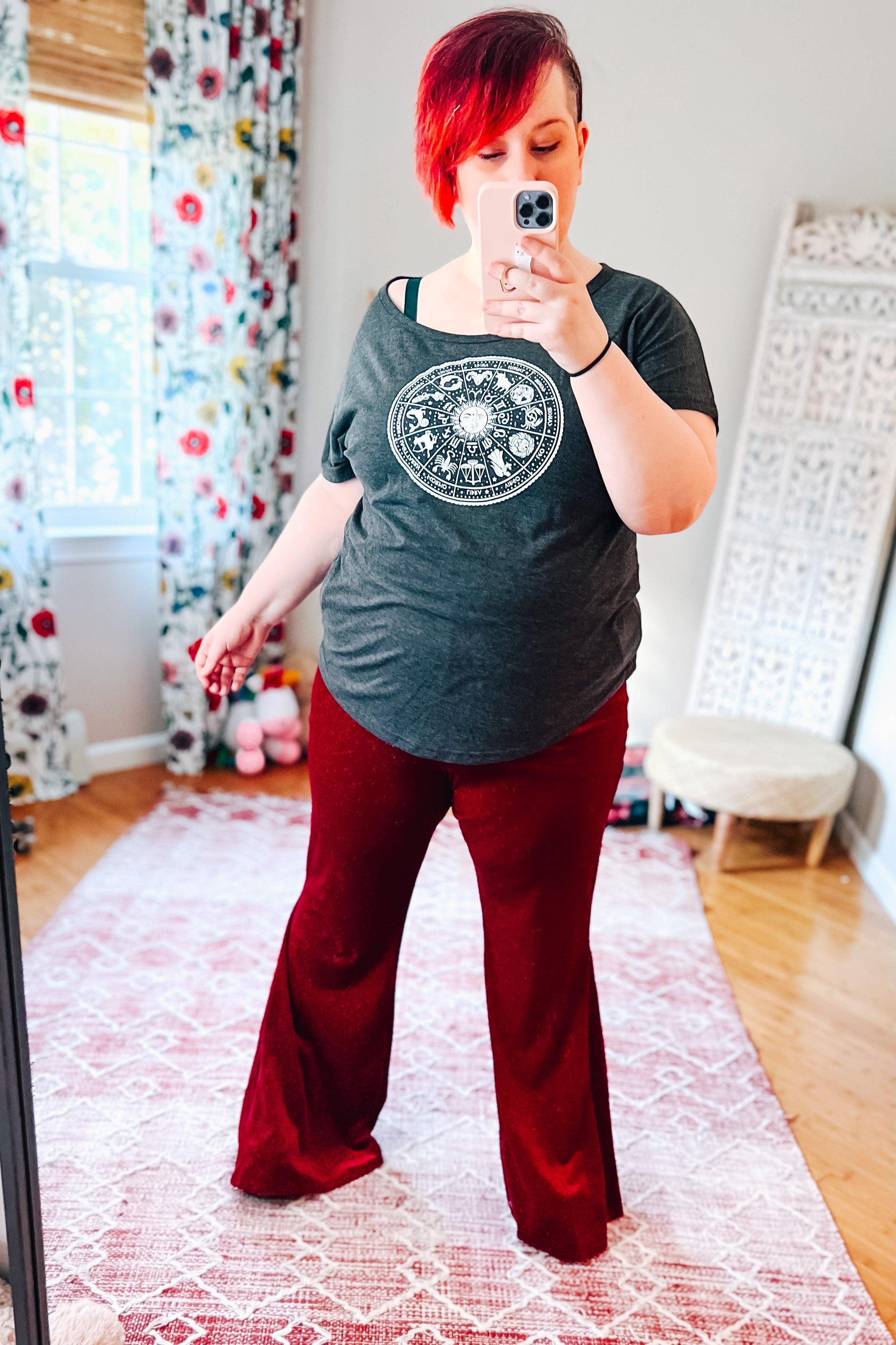 Woman taking mirror selfie wearing ruby red velvet flare bell bottoms and dark gray zodiac graphic tee in sunlit room