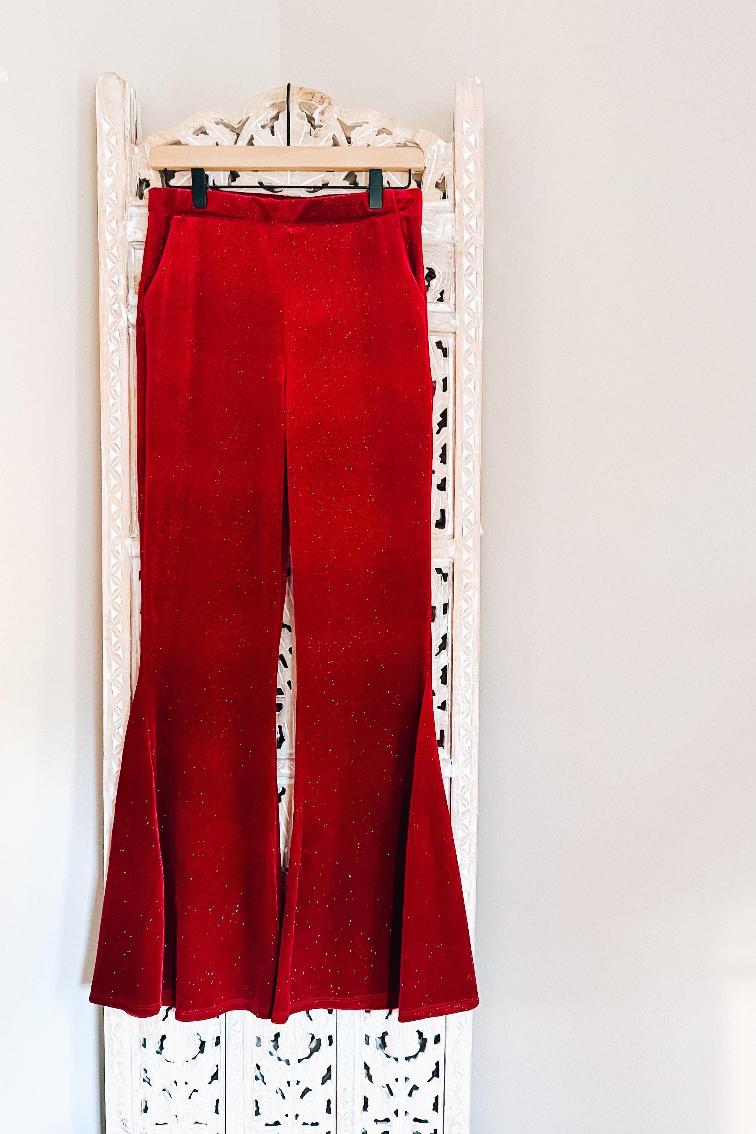 Ruby red velvet bell bottoms with subtle glitter accents hanging on carved white wooden hanger panel