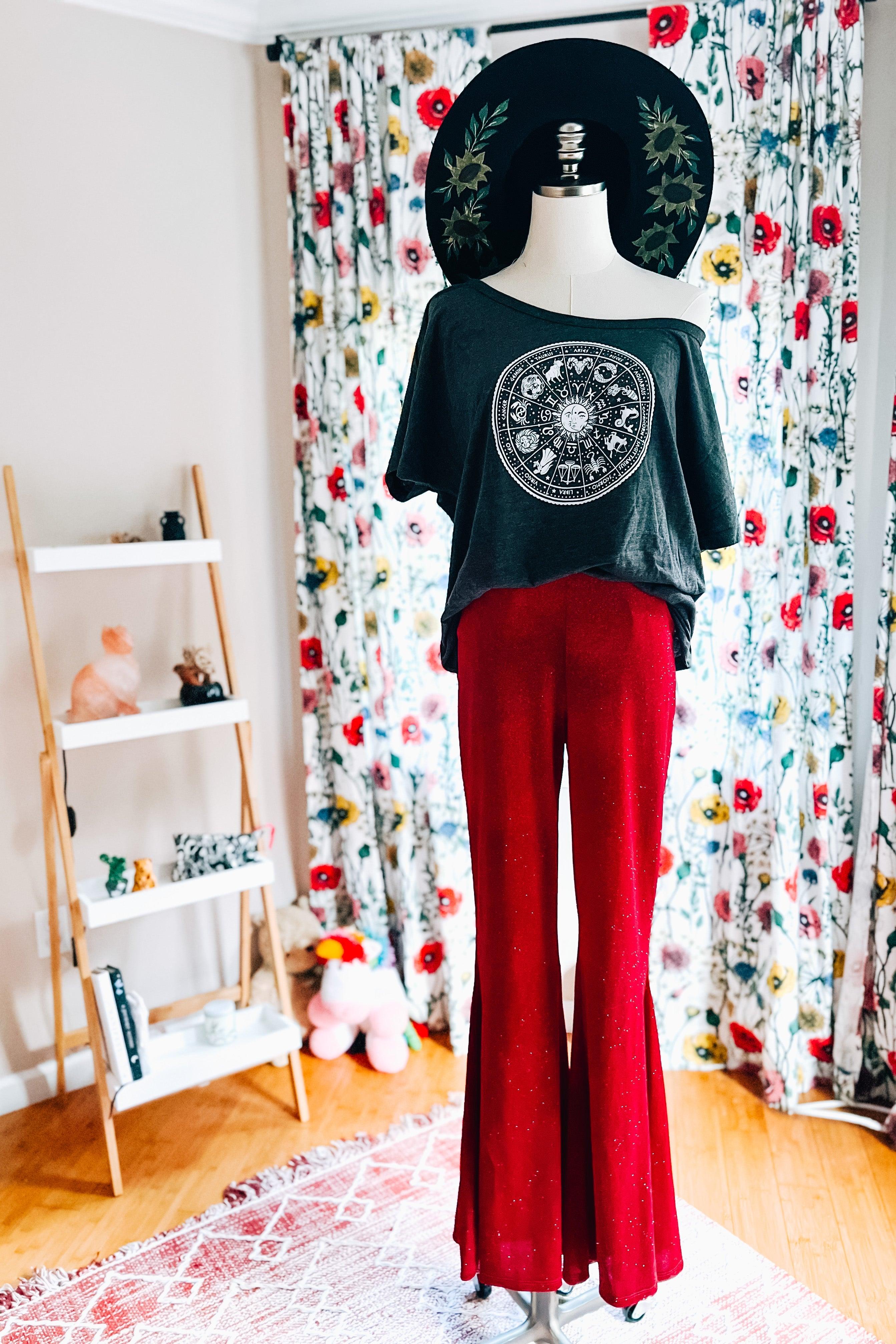 Mannequin dressed in ruby red glitter bell bottoms and black off-shoulder graphic top with wide-brim hat in bright room