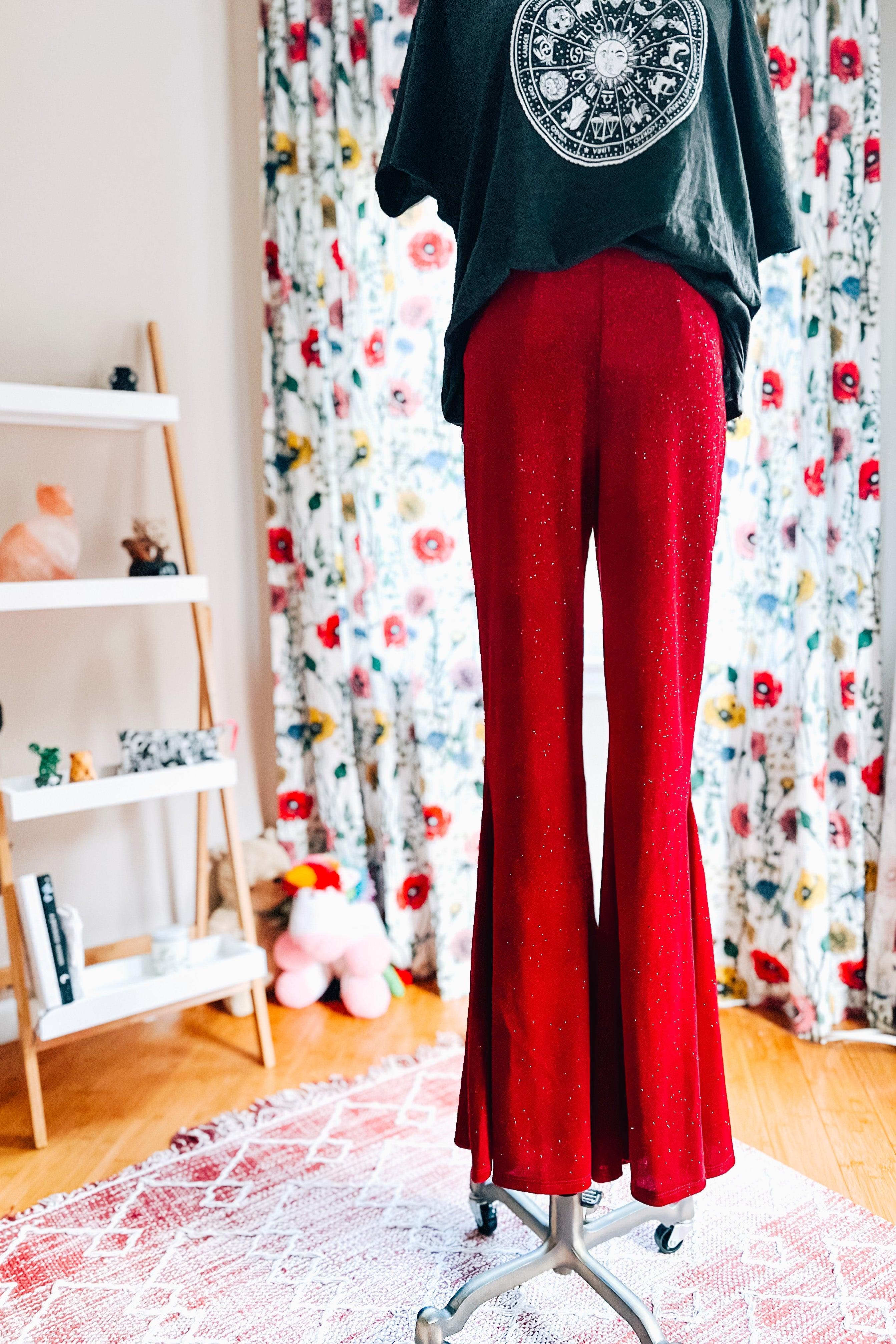 Bright ruby red glitter bell bottoms with flare legs displayed on mannequin in cozy room with floral curtains