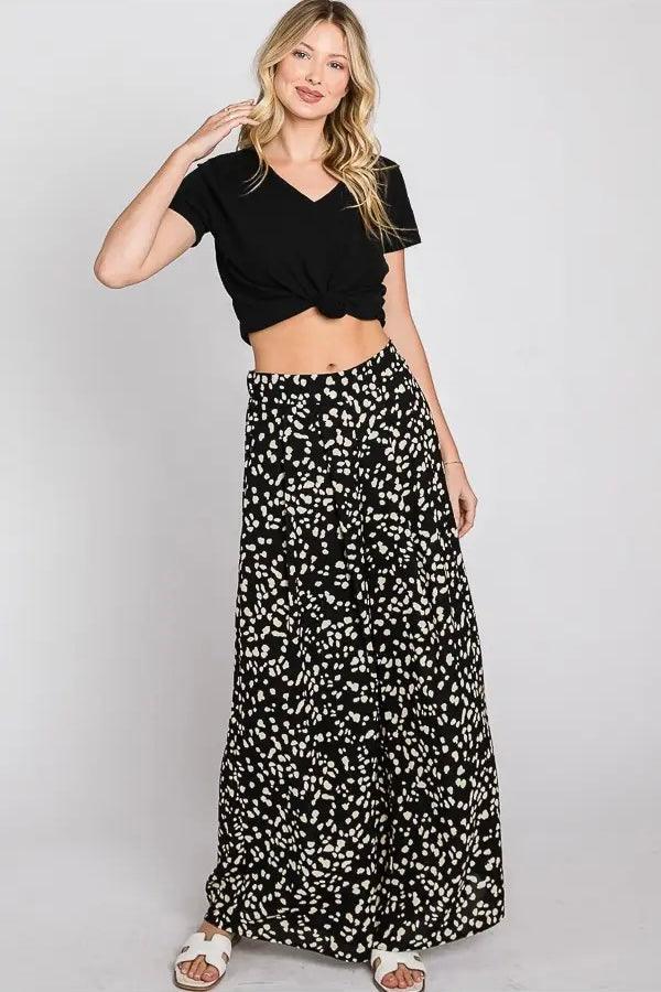Woman wearing black wide leg pants with white irregular Dalmatian spots paired with knotted black crop top and white sandals