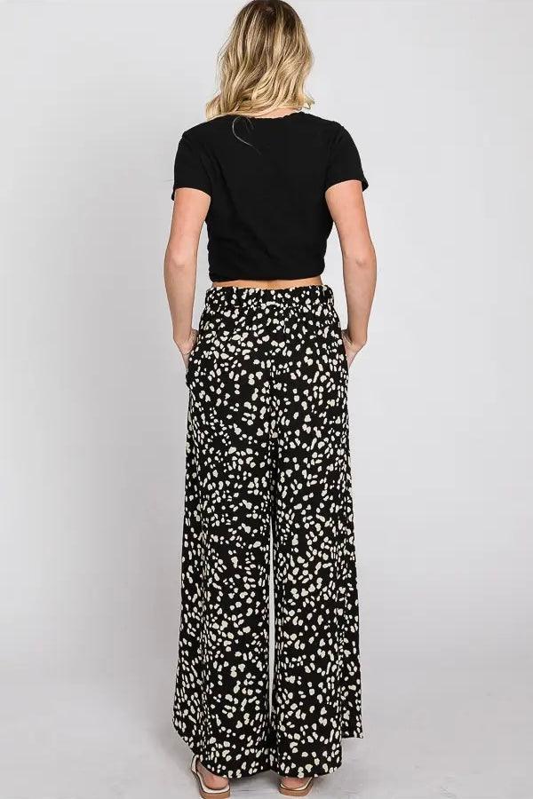 Woman wearing black wide leg pants with white Dalmatian dots paired with black short sleeve top viewed from back