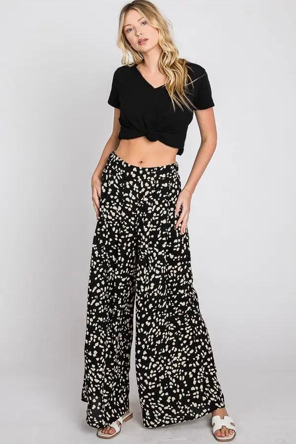 Woman wearing black Dalmatian print wide leg pants paired with a knotted black cropped tee and white sandals