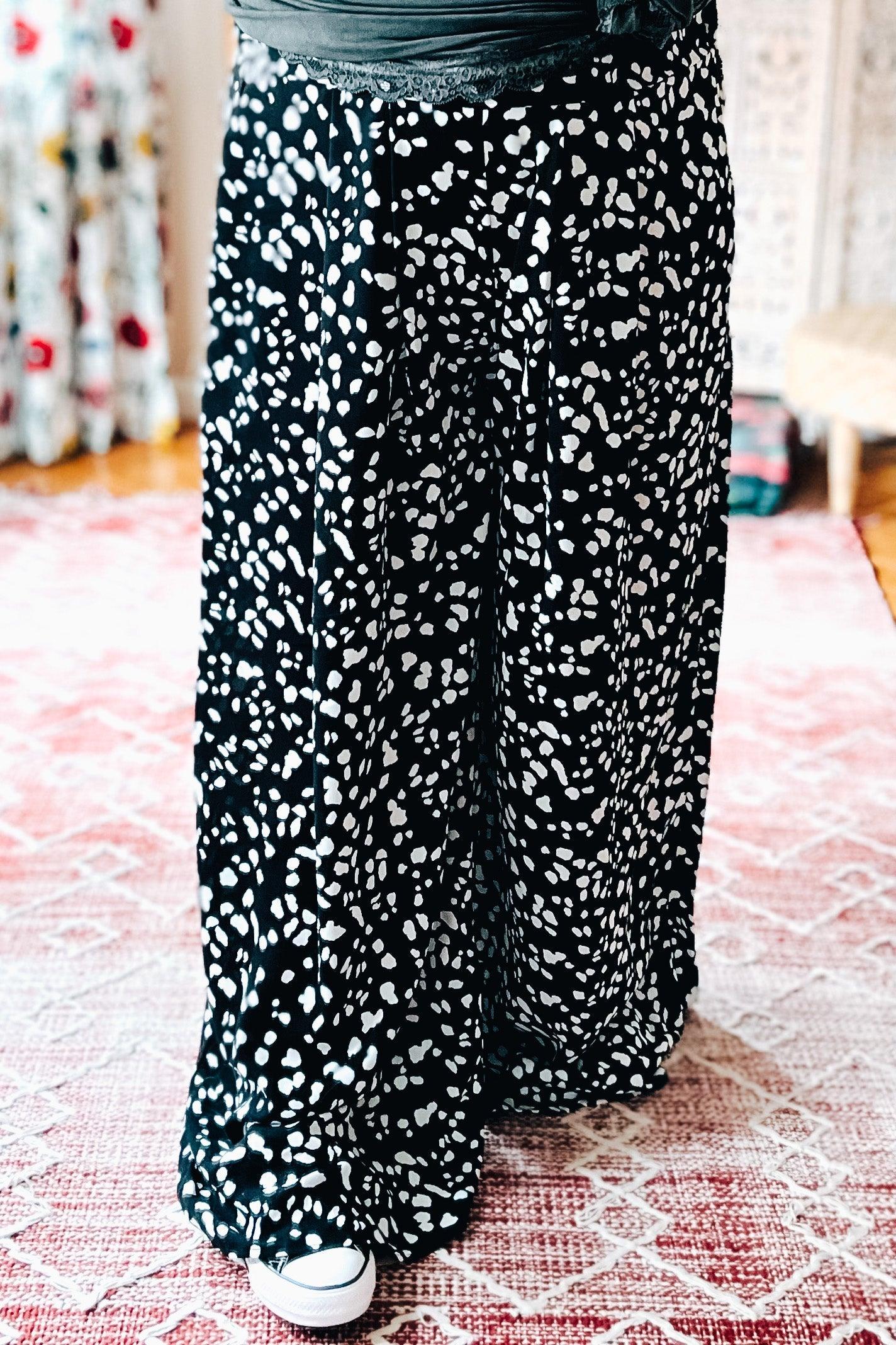 Black wide leg pants with scattered white irregular spots styled with white sneakers on pink patterned rug